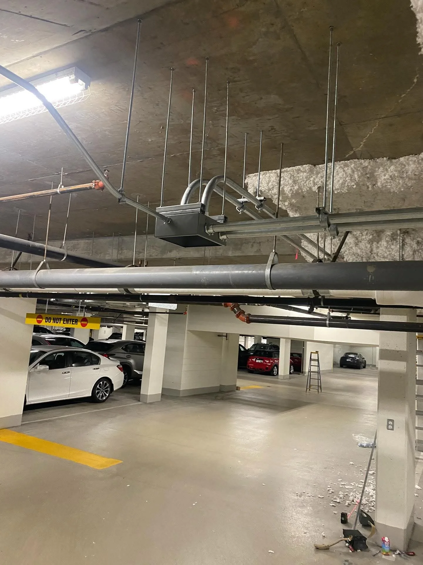 Underground parking garage with parked cars, construction materials, and a yellow 'Do Not Enter' sign on a column.