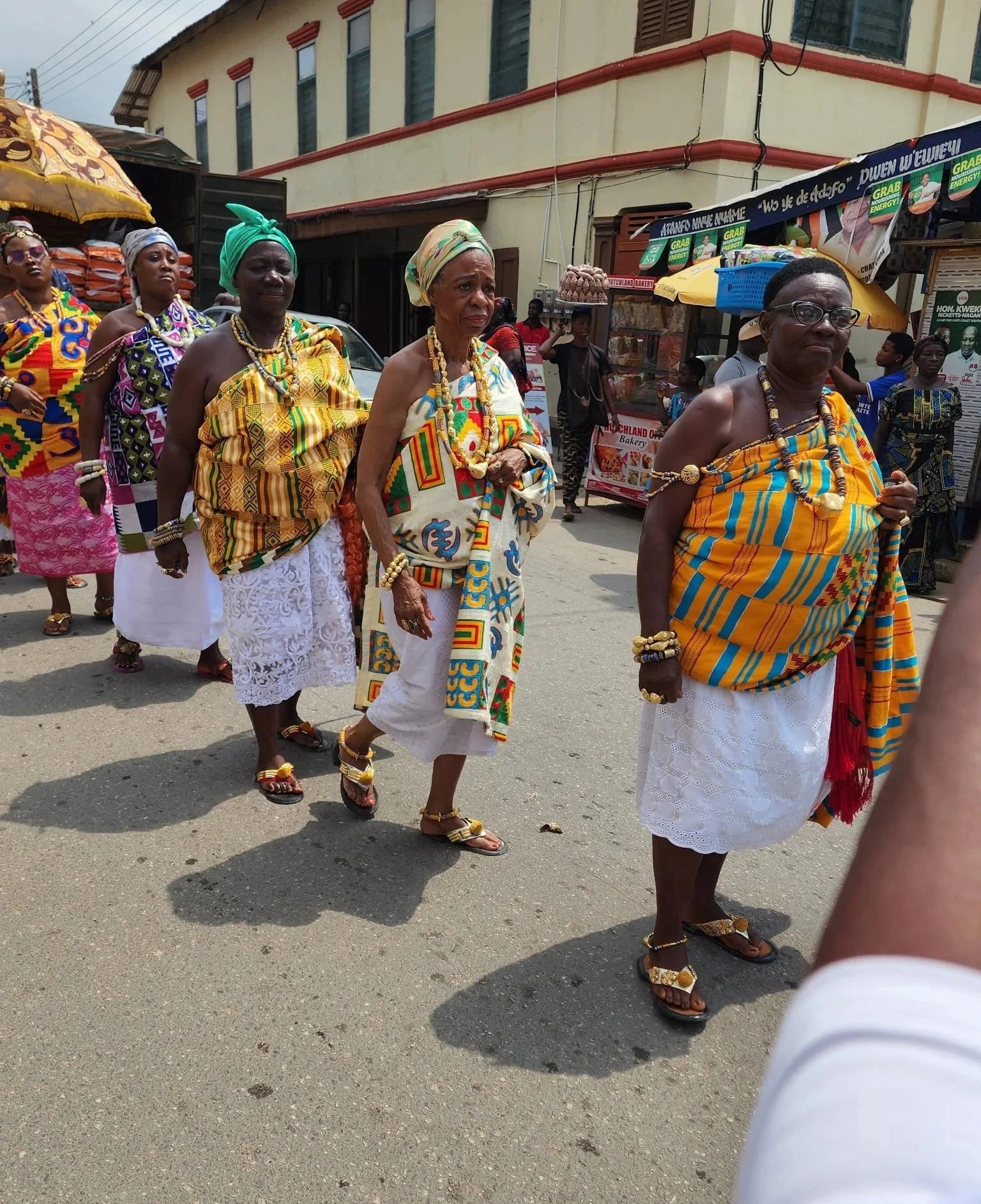 Women dressed in traditional African clothing and jewelry participating in a cultural parade on a city street.