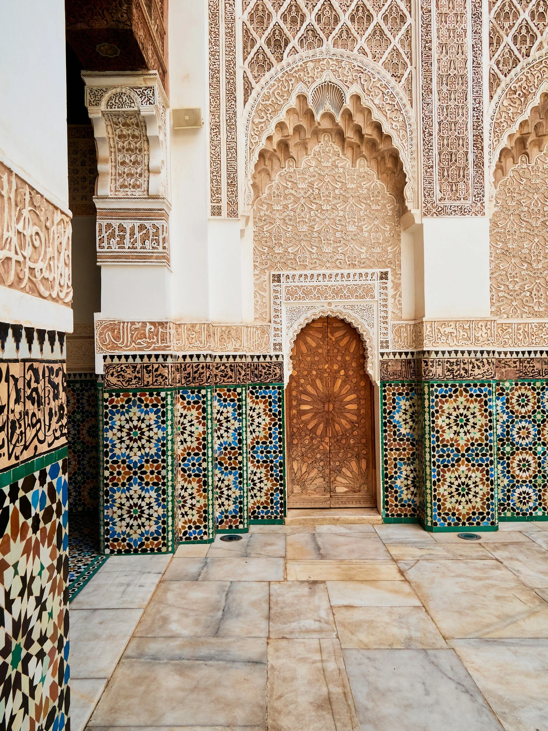 Intricate Moroccan-style architecture with carved plaster walls, colorful tilework, and a wooden door.