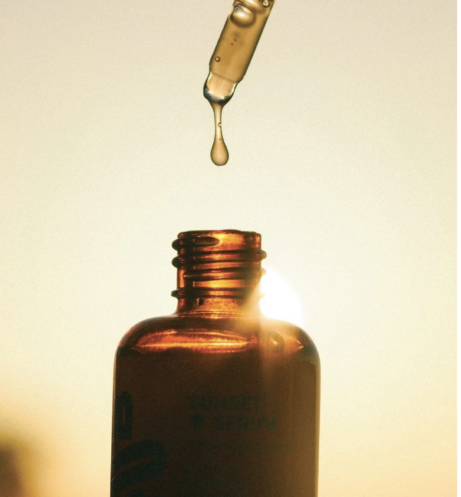 A dropper releasing liquid into a small brown bottle with the sunset in the background.