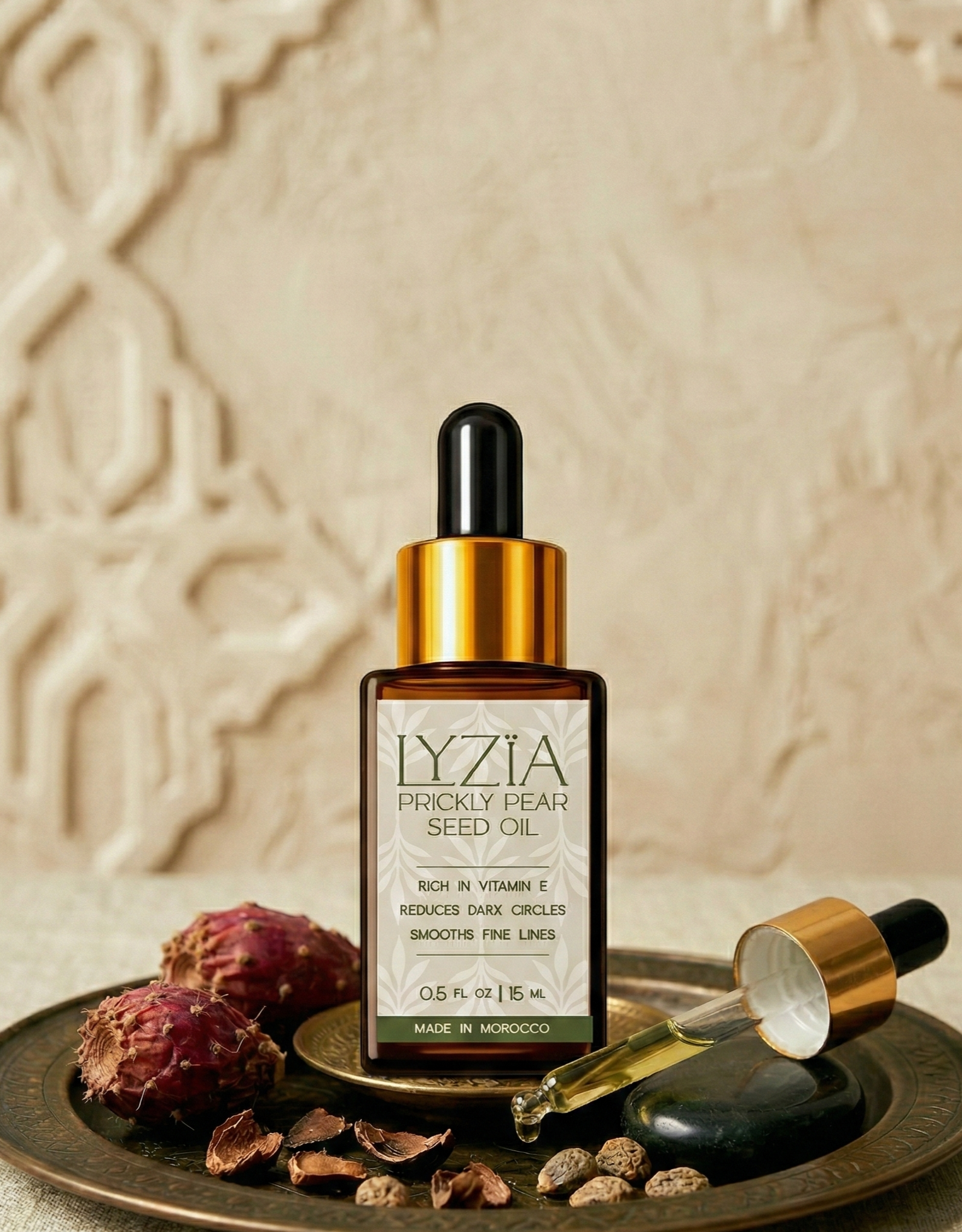 A bottle of LYZIA Prickly Pear Seed Oil with a dropper, placed on a decorative tray along with prickly pear fruits, seeds, and a stone.