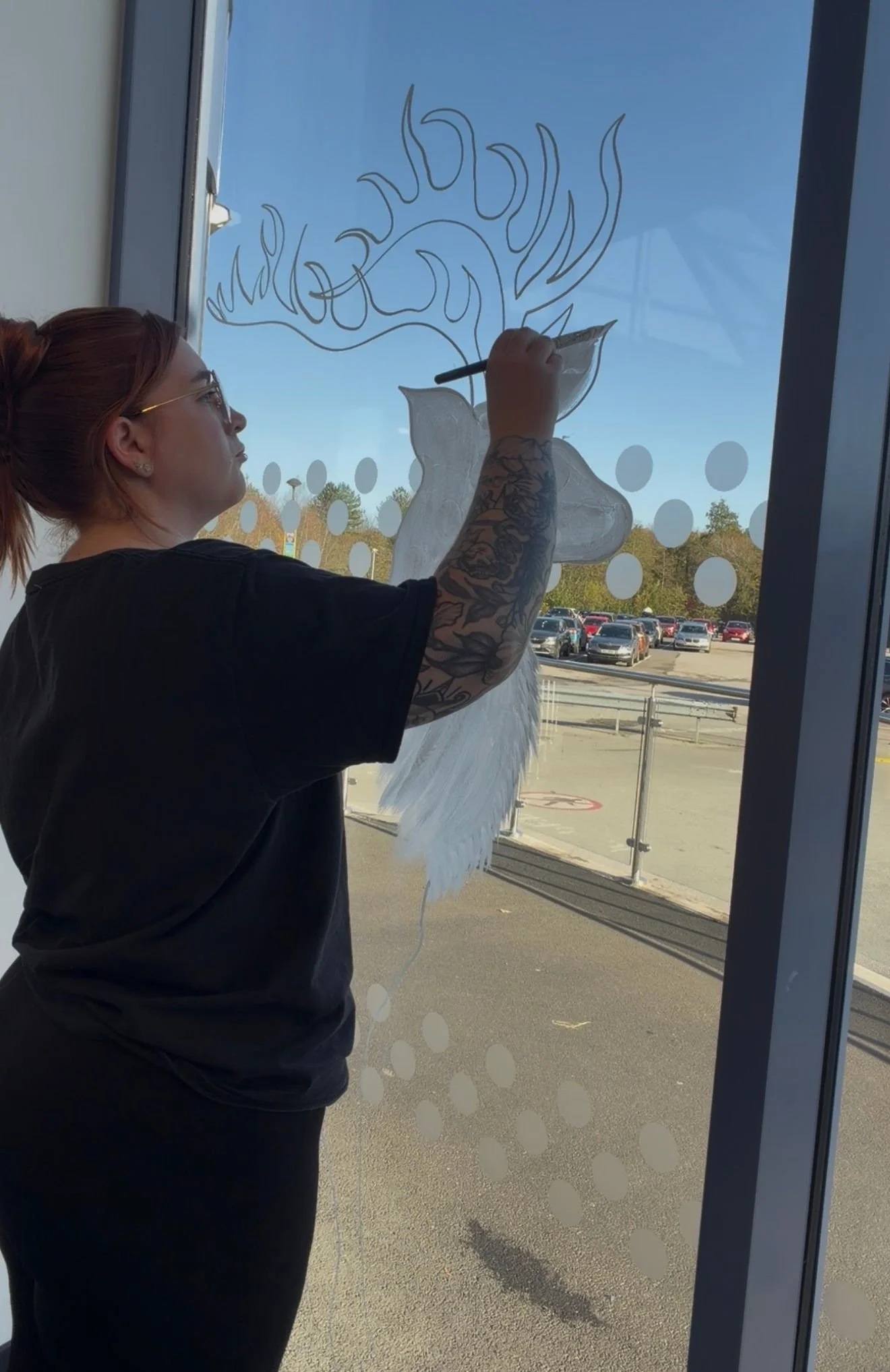 Woman with tattoos painting a unicorn with flames on a glass window.