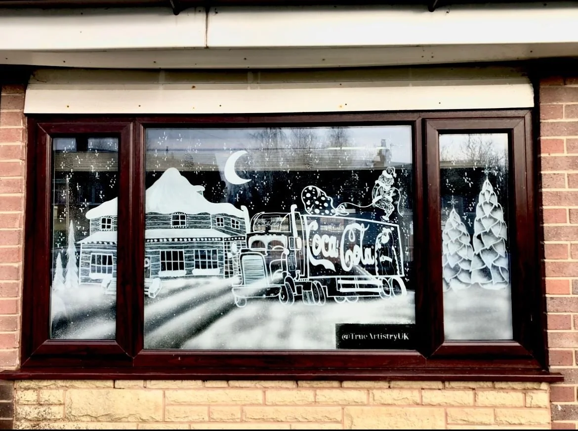 Decorative window art depicting a mountain, a crescent moon, snow-covered trees, a house, a truck with Coca-Cola branding, a skier, and snowflakes.