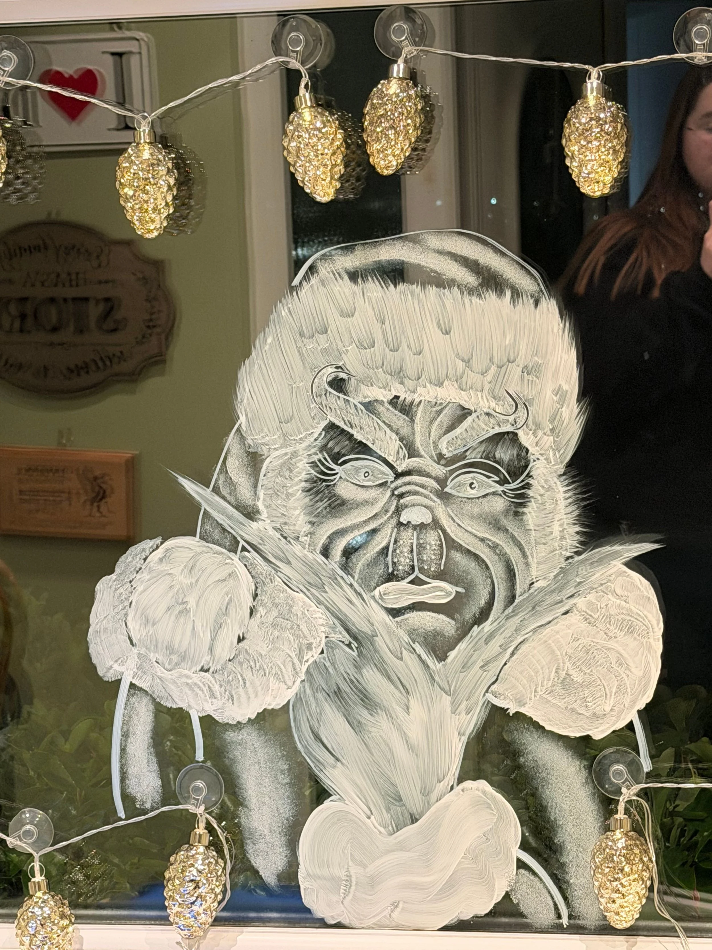 Decorative window with a painting of a fierce creature with a horned, furry appearance, surrounded by string lights shaped like pinecones.