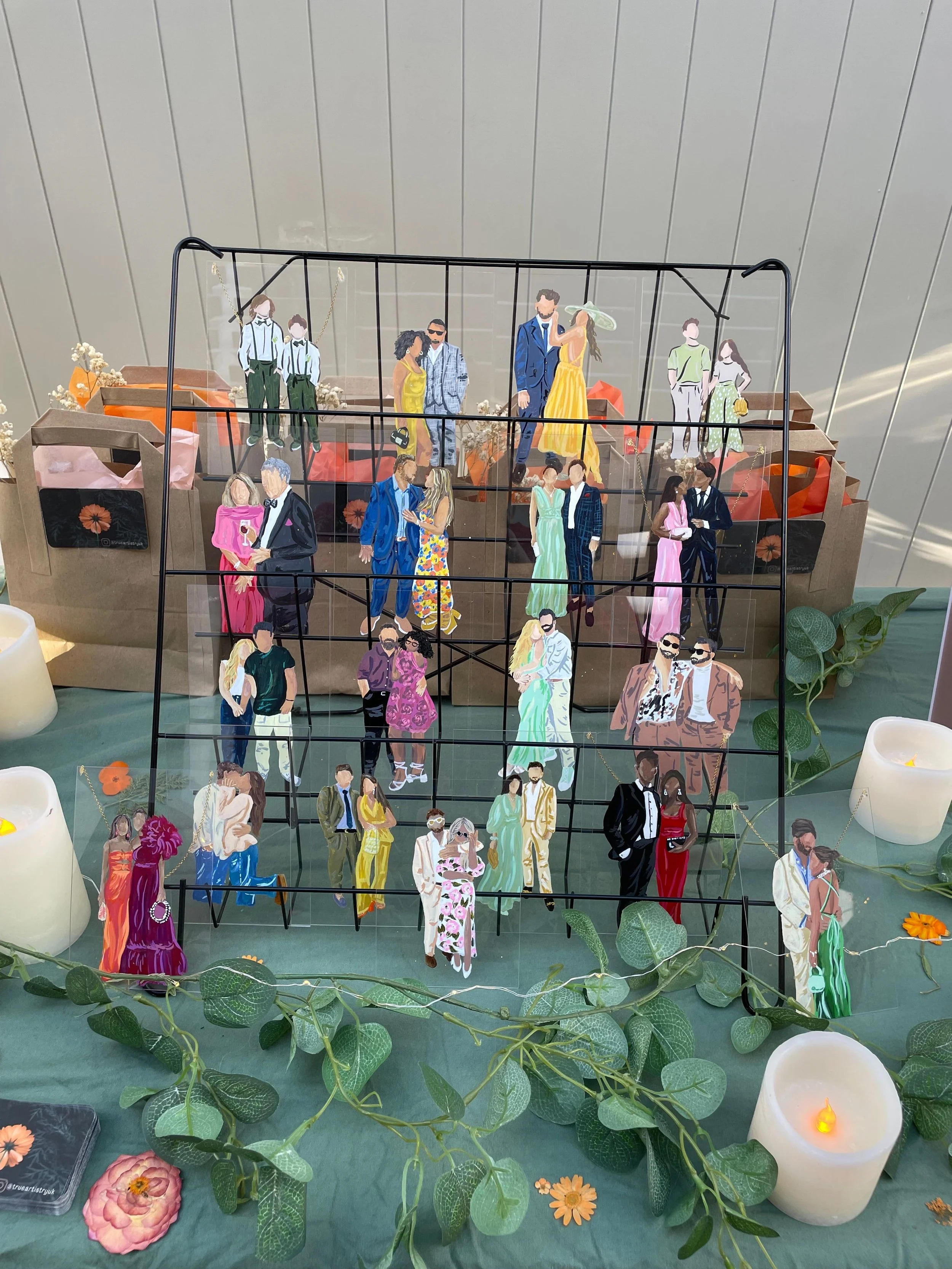 Decorative display of miniature paper cutout figures of people on a multi-tiered stand, surrounded by flowers and candles.