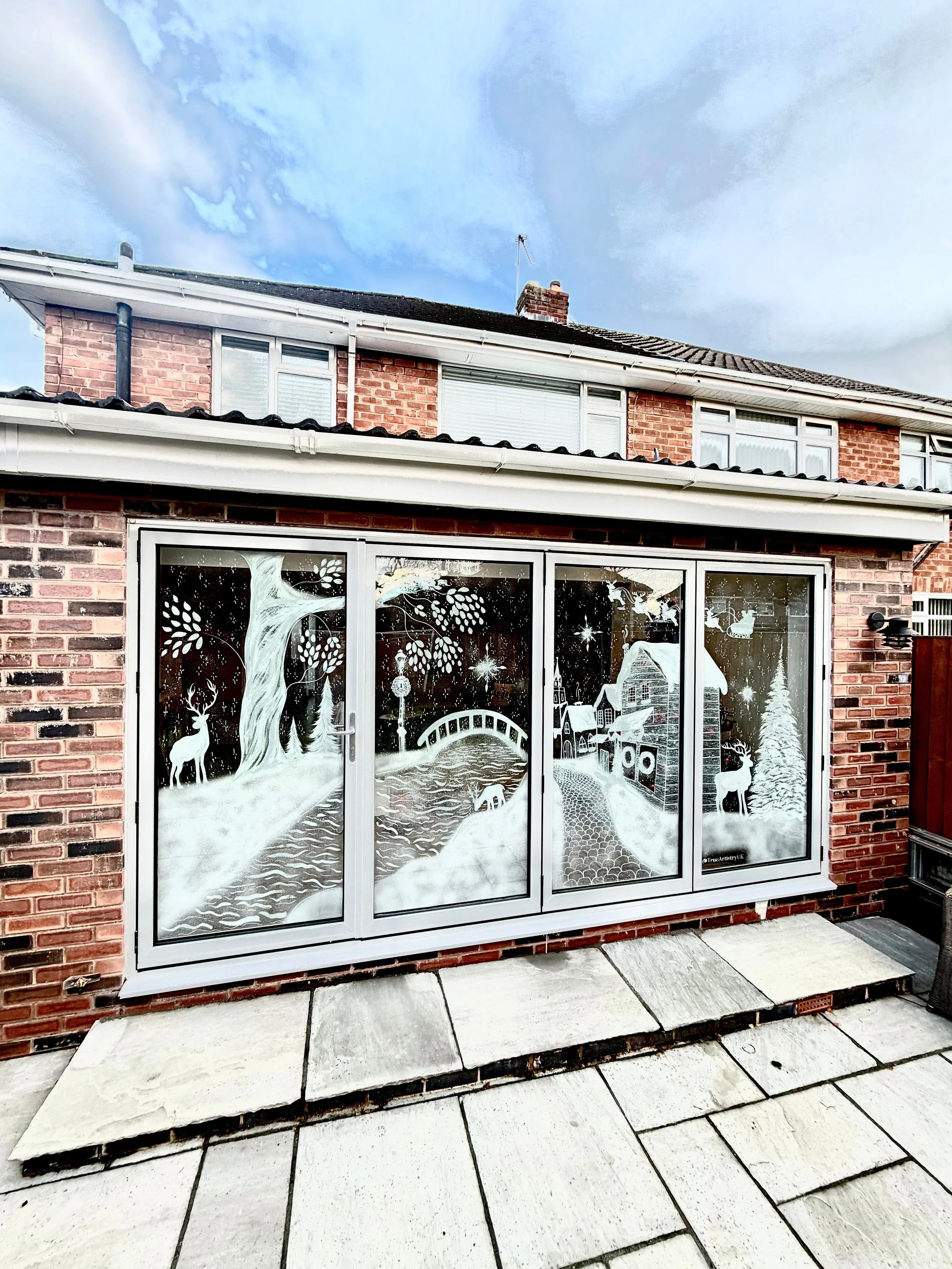 Decorative winter scene on glass door depicting a snow-covered landscape with trees, deer, and a small village with houses and a church, all rendered in white.