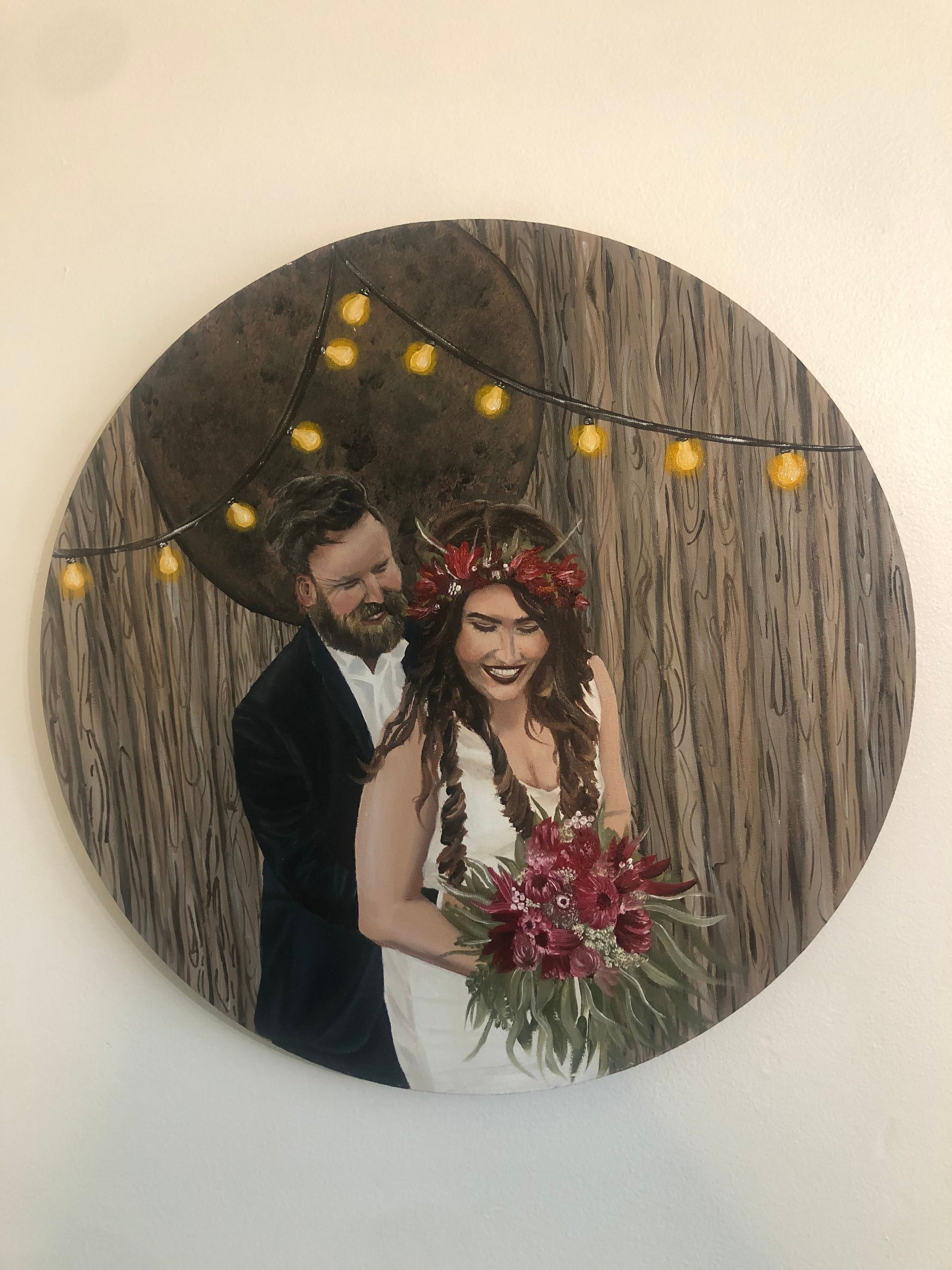 A painting of a smiling couple in wedding attire, with the bride holding a bouquet of red flowers and the groom standing behind her. They are in front of a wood-paneled wall with string lights and a large decorative object above their heads.