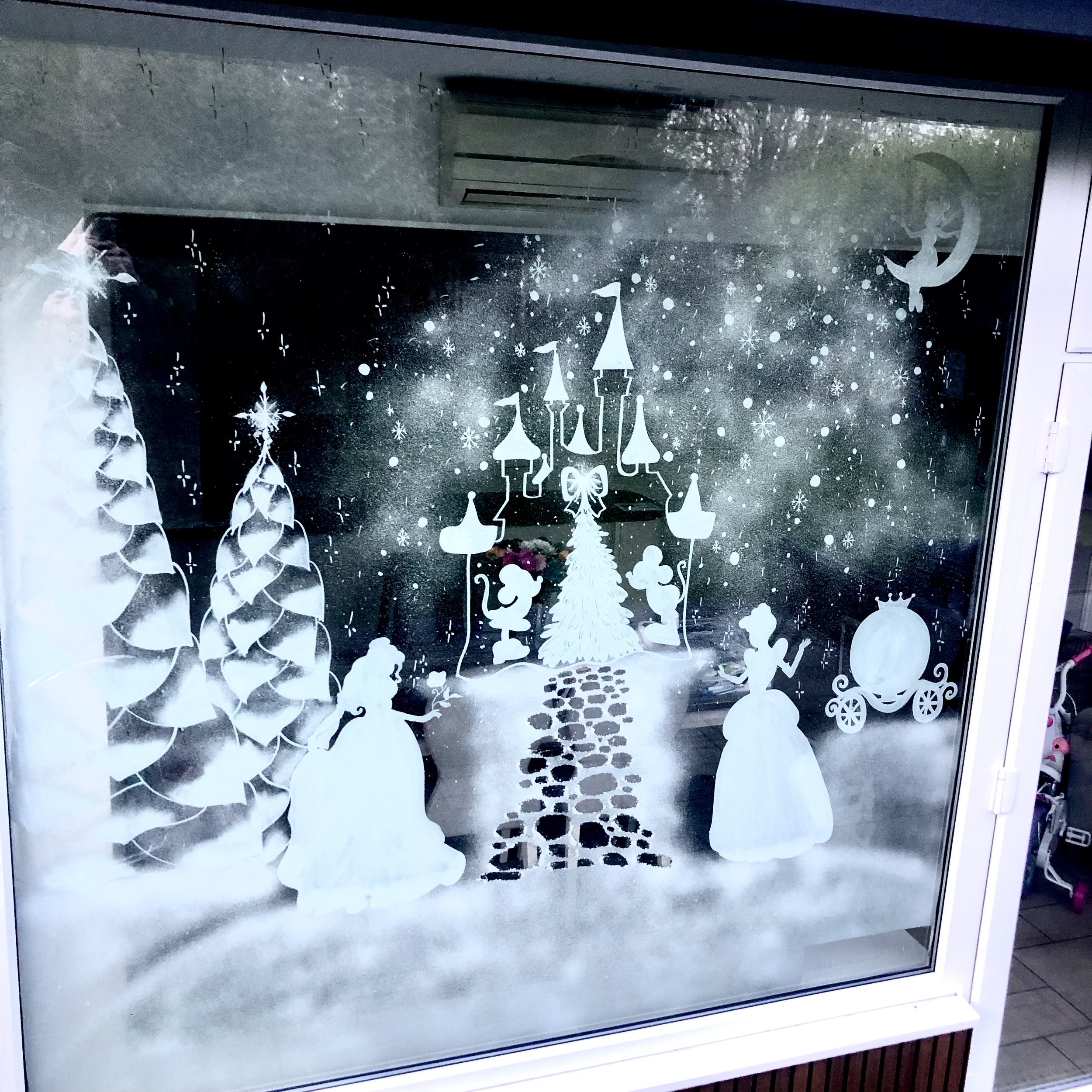 Snowy window decoration featuring a Christmas castle, Christmas trees, two women in dresses, an ornament cart, and a starry night sky
