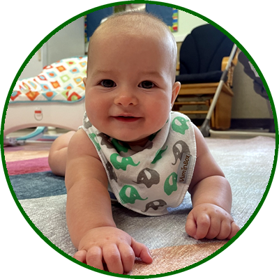 Baby lying on the floor smiling, wearing a colorful sleeveless shirt with dinosaur prints.