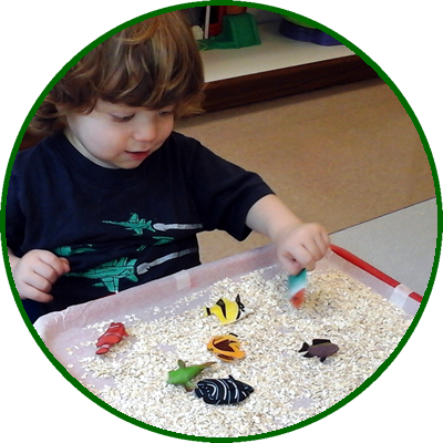 A young child playing with toy fish in a mini aquarium filled with white rice.