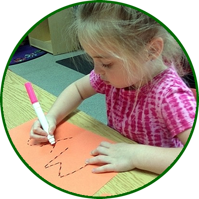 Young girl with blonde hair in a pink shirt writing on orange paper with a pink marker.