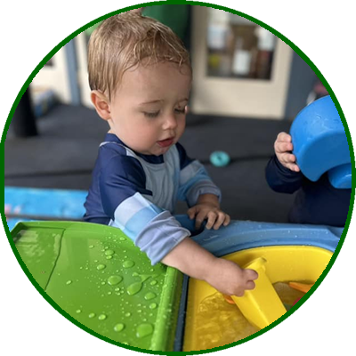 Young child playing at a water table outdoors, touching water with his finger.
