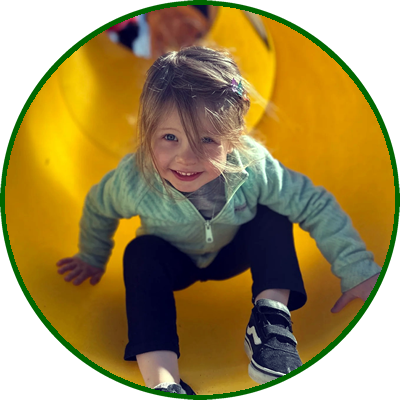 Child smiling and crawling inside a yellow playground slide.