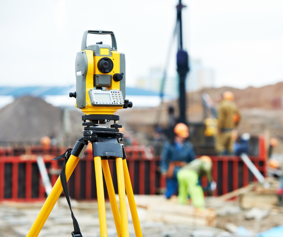 Théodolite jaune sur un trépied sur un site de construction avec des ouvriers en arrière-plan. Service d'arpentage