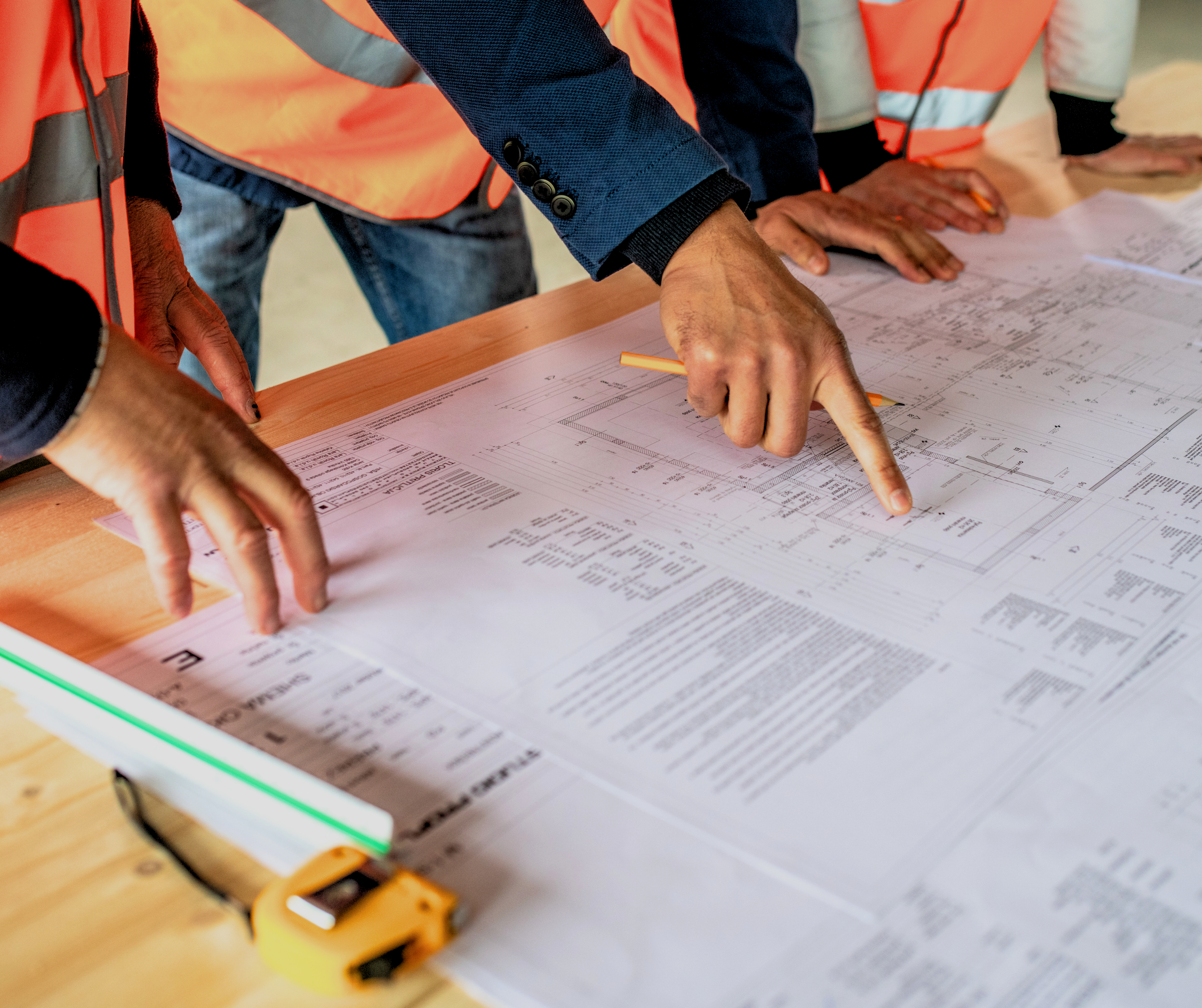 Groupe de personnes portant des gilets de sécurité orange, examinant des plans ou des schémas sur une table.