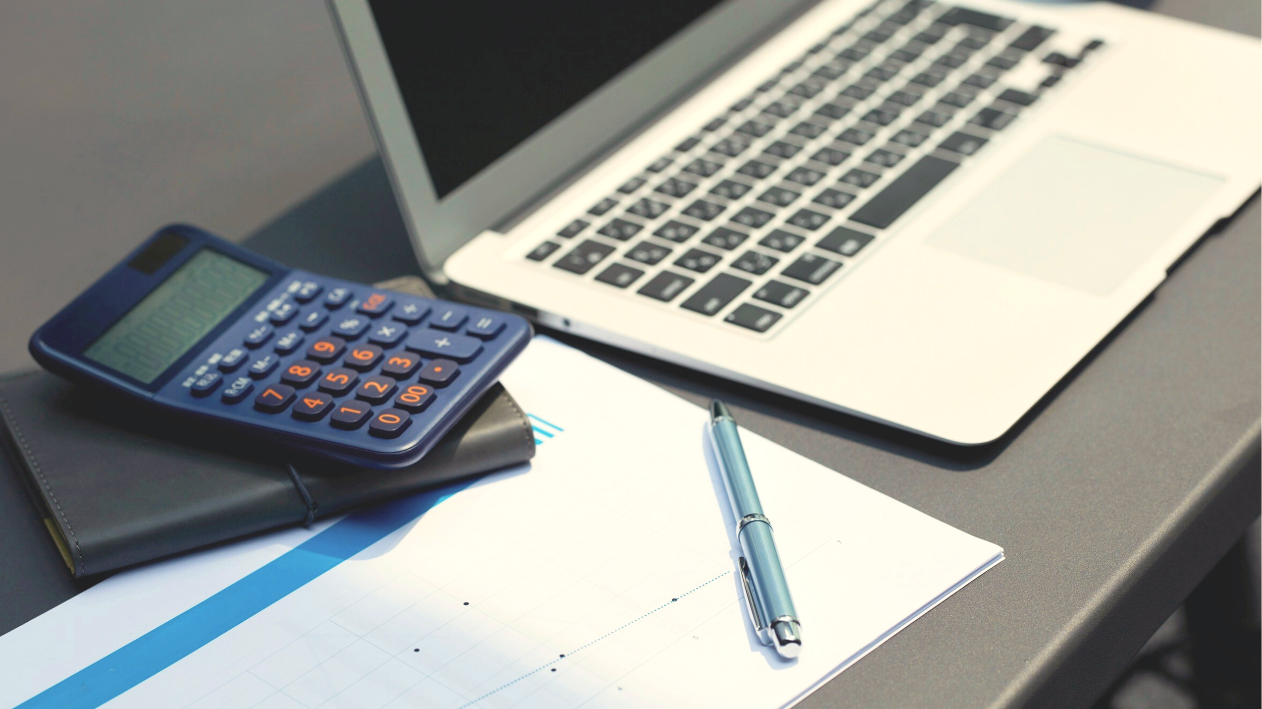 Un ordinateur portable, une calculatrice, un stylo, des papiers et un carnet sur un bureau.