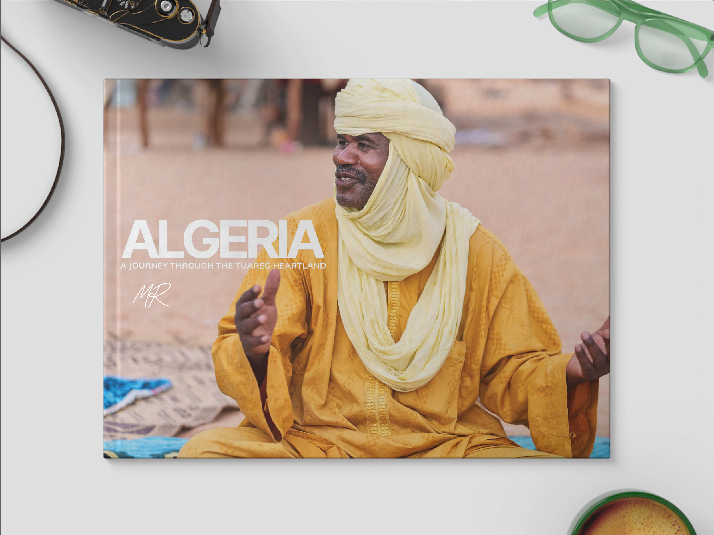 Cover of a travel book titled 'Algeria: A Journey Through the Tuareg Heartland' featuring a smiling Tuareg man in traditional yellow clothing and turban, sitting outdoors with a desert background.