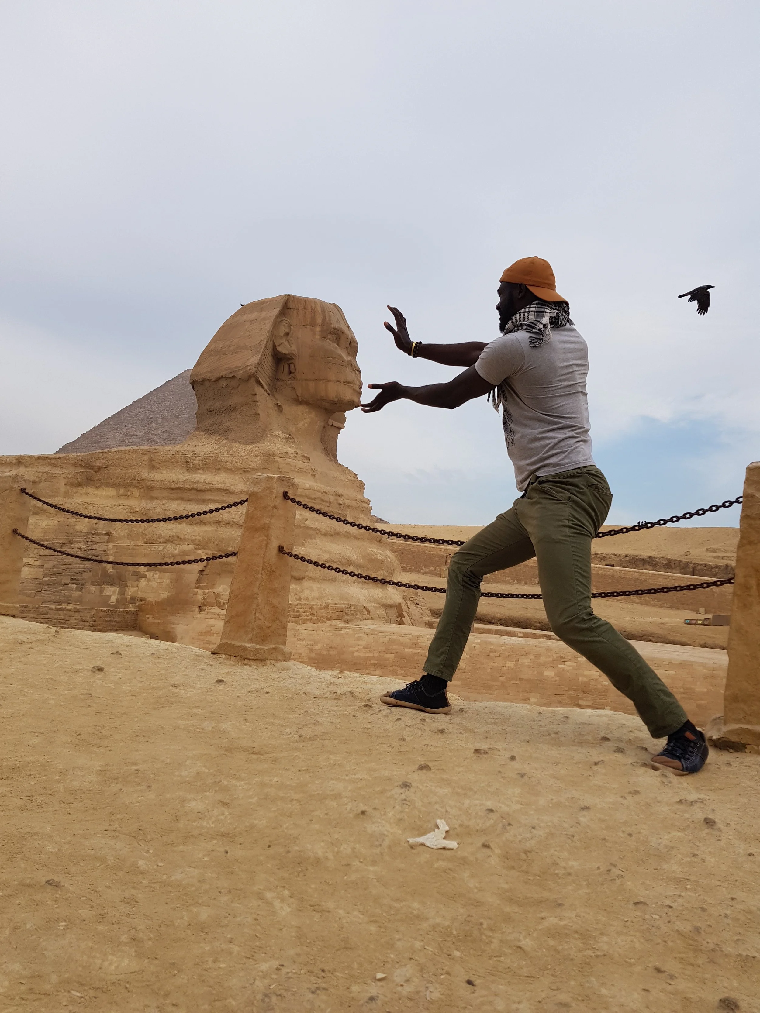 A person appears to be pushing or holding the head of a large stone sphinx statue in the desert near a pyramid in Egypt.