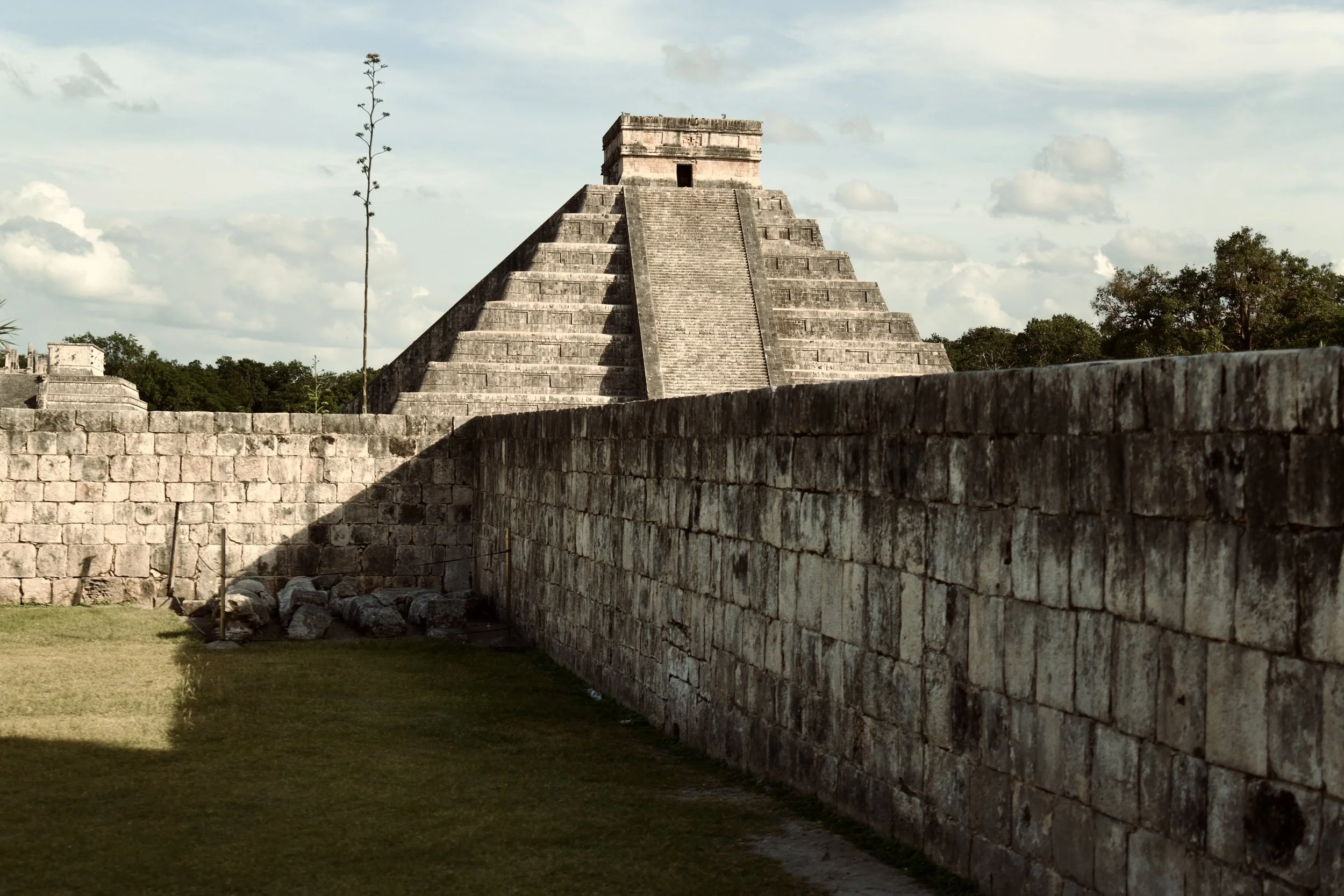 Ancient Mayan pyramid in a jungle setting with stone walls and steps leading up to a temple, under a partly cloudy sky.