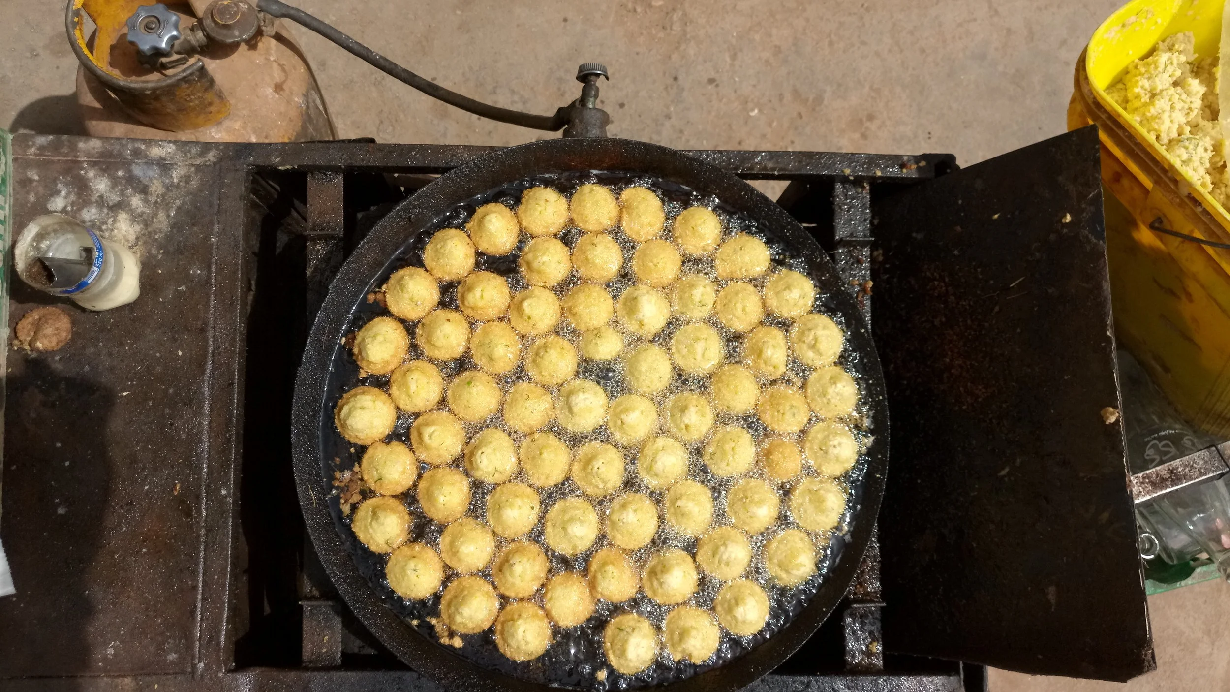 Frying small, round, golden-brown snacks in a black cast iron skillet over oil, on a stovetop.