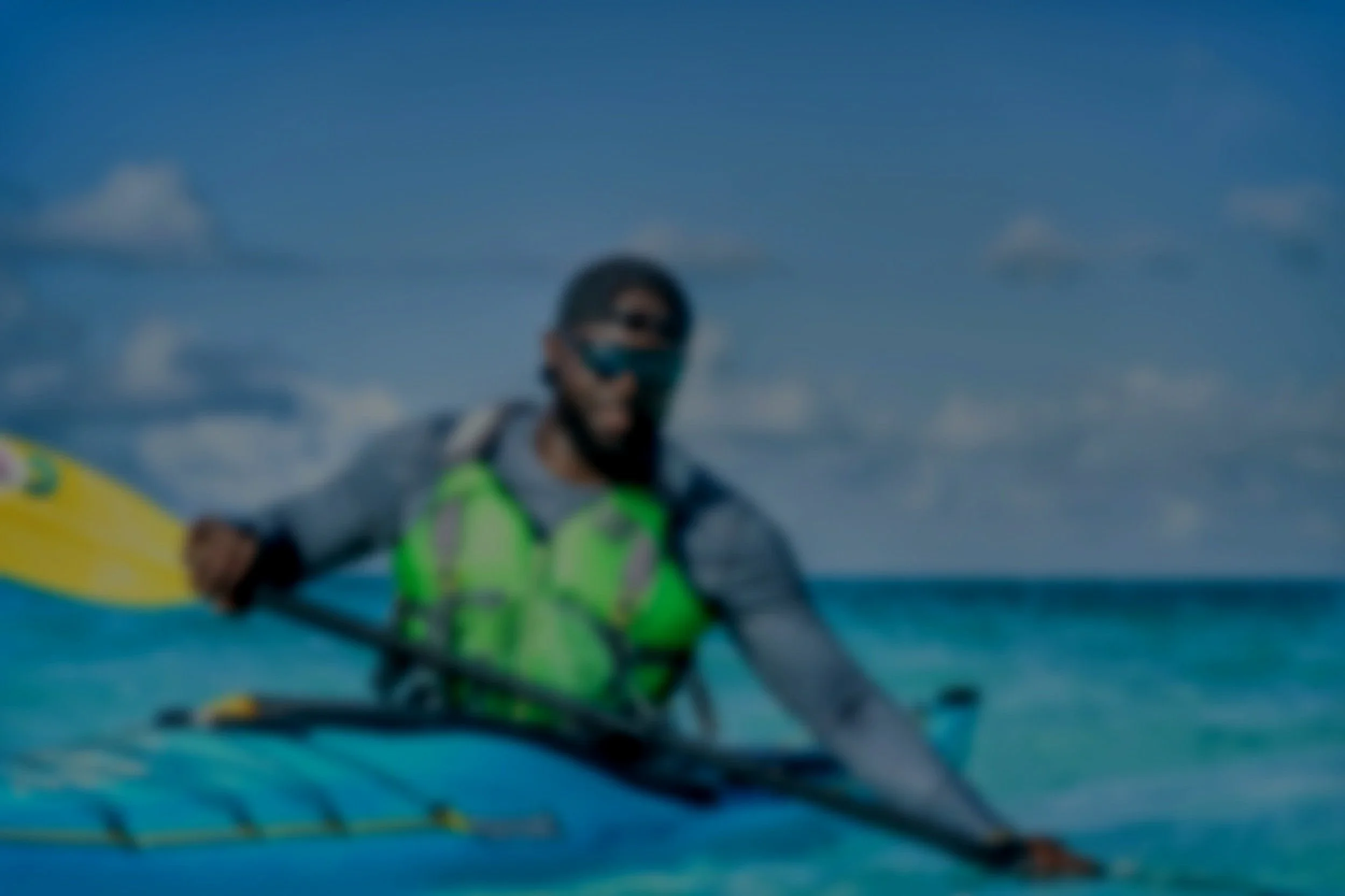 A person kayaking on the ocean with a sunny sky and scattered clouds in the background.