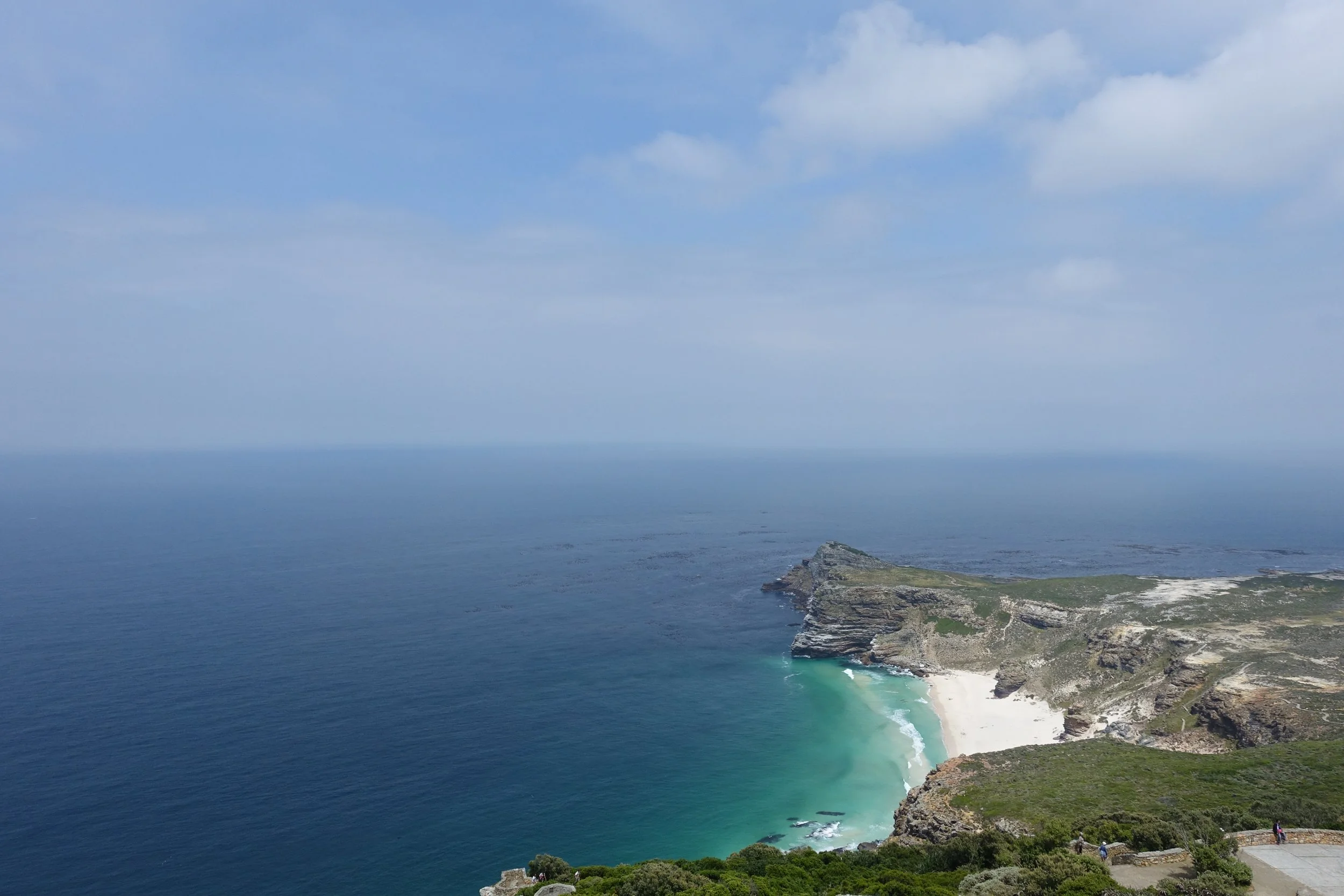 A scenic view of a coastline with cliffs and a beach, overlooking the ocean under a partly cloudy sky.