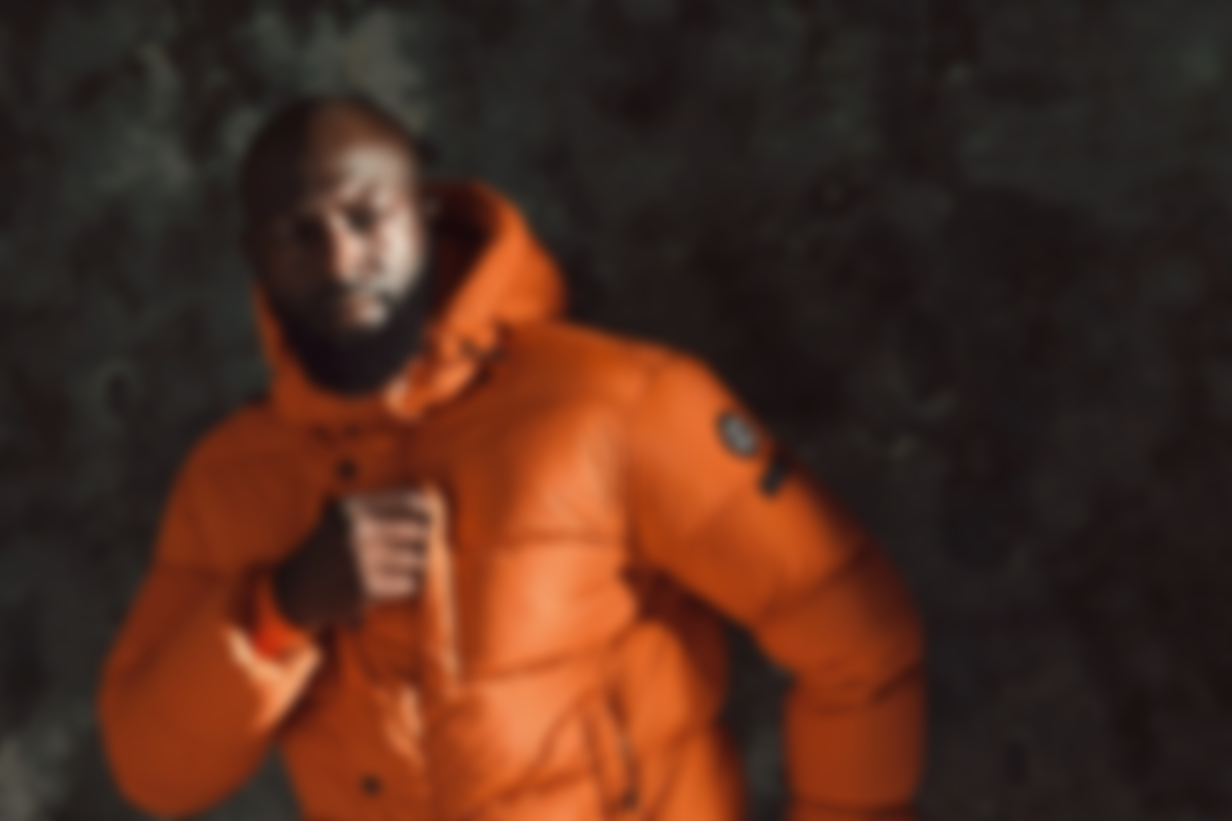 Blurry photo of a man wearing an orange jacket, lying on the ground and looking up at the camera.