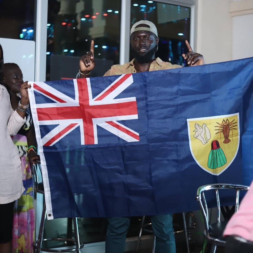 Man wearing a beige cap holding the flag of Fiji at a social gathering