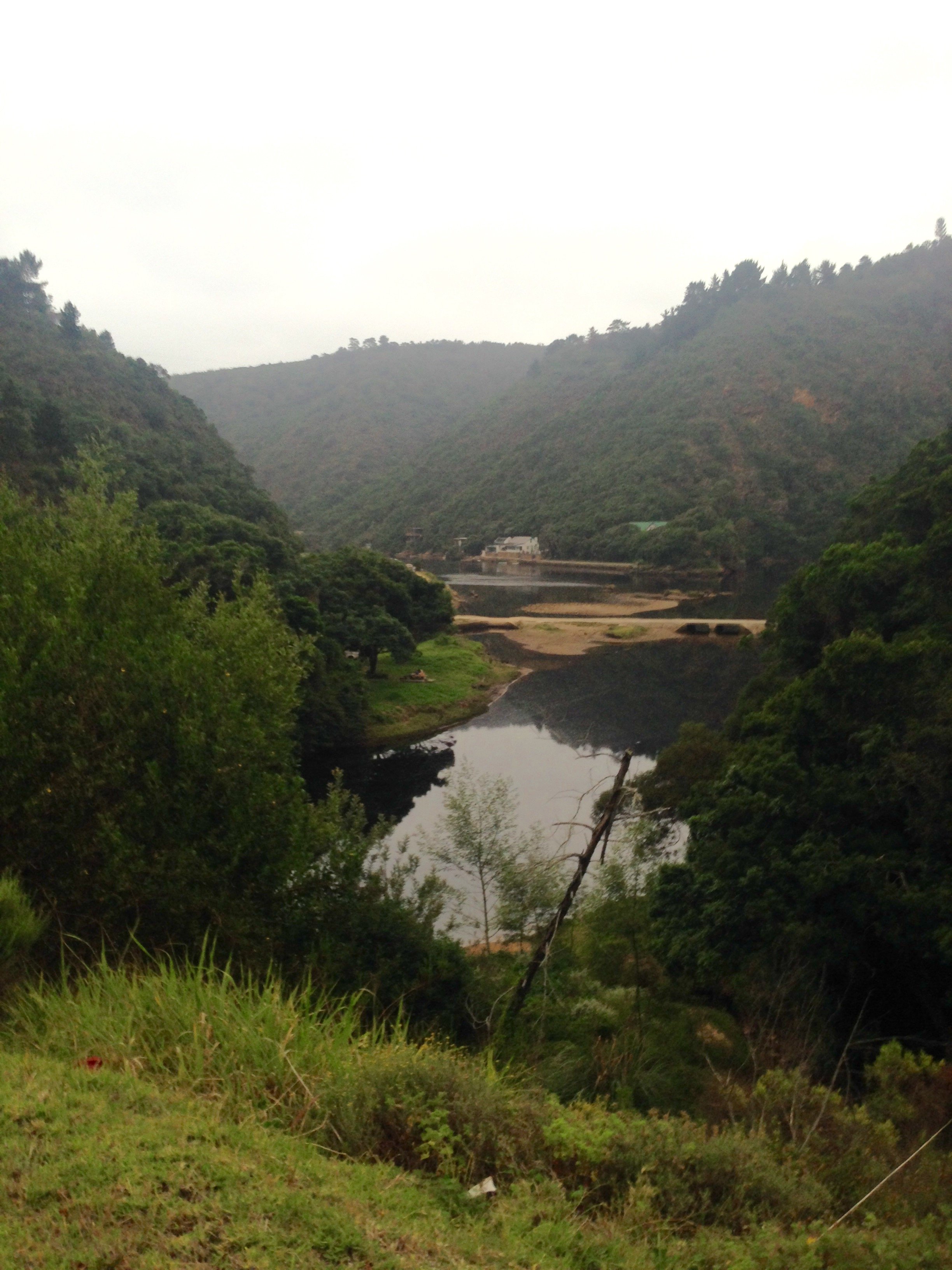 Scenic view of a river flowing through a valley with lush green hills and a cloudy sky.