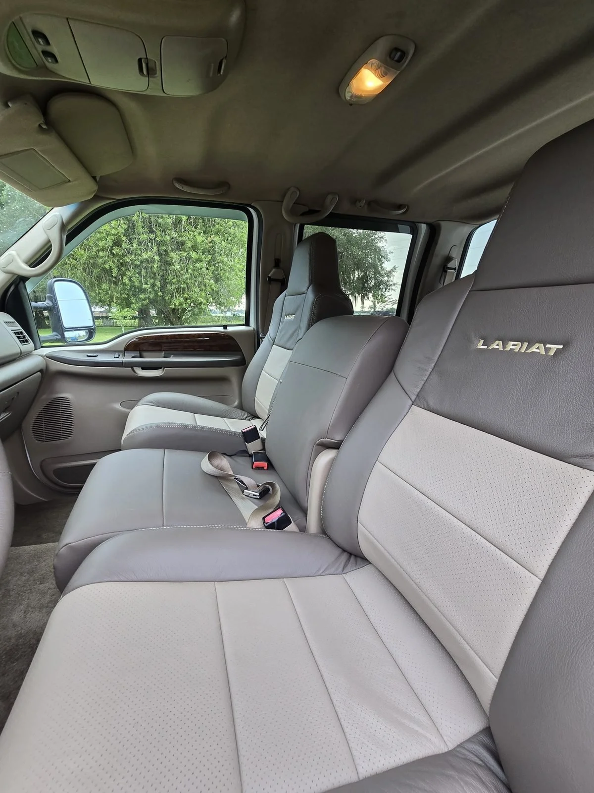 Front bucket seats in two-tone taupe and light tan perforated leather with LARIAT embroidered on the seat backs, in a Ford Super Duty crew cab
