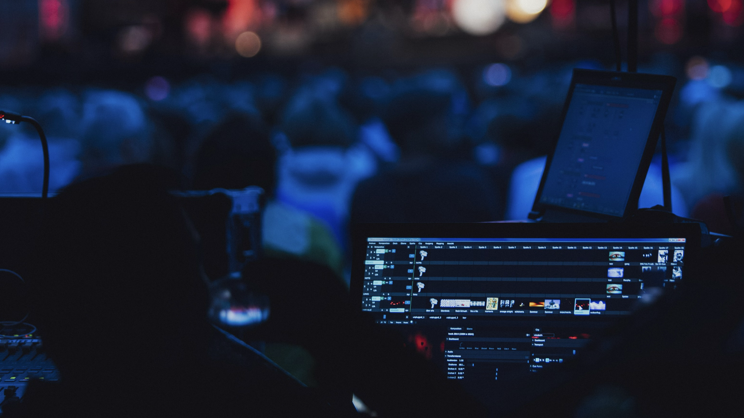 Pantalla de ordenador con software de edición de video, en un entorno oscuro y con muchas personas sentadas, probablemente en un evento en vivo o concierto.