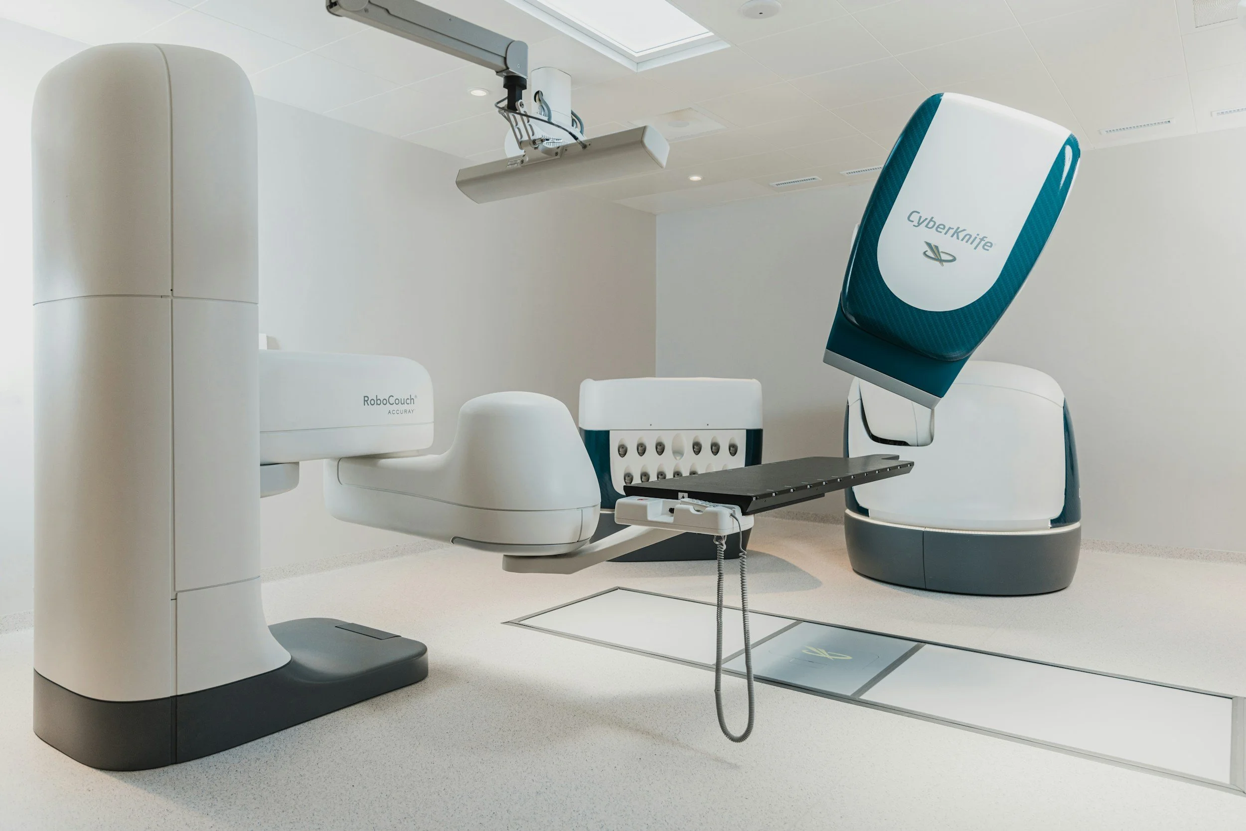 Sala de procedimientos médicos con equipo avanzado, incluyendo un robot quirúrgico y un láser CyberKnife para tratamientos precisos.