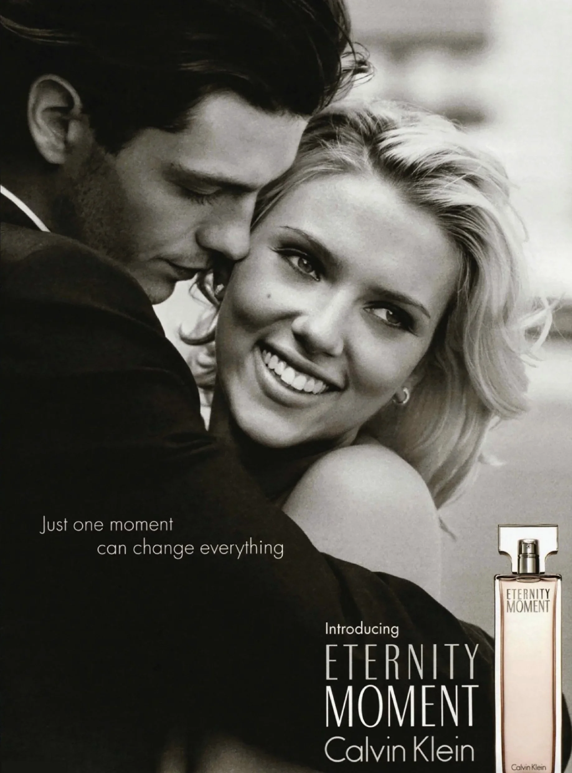 A black and white photograph of a man and woman in an intimate pose, with the man resting his forehead against the woman's head. The woman has blonde hair and is smiling, while the man has dark hair and closed eyes. The image includes text promoting 