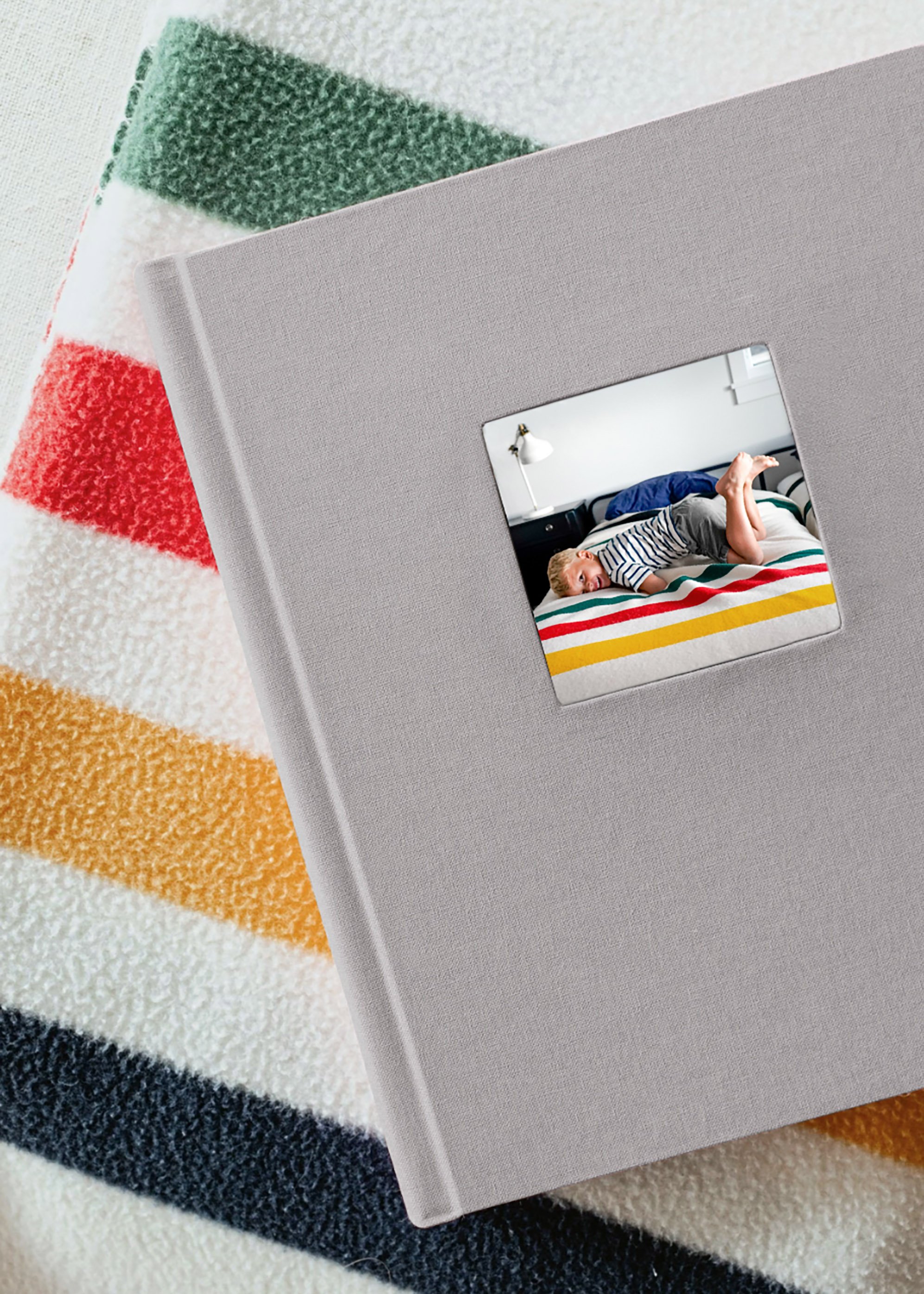 A photo of a photo frame on top of a multicolored rug, showing the reflection of a bed with striped bedding and a nightstand with a lamp.