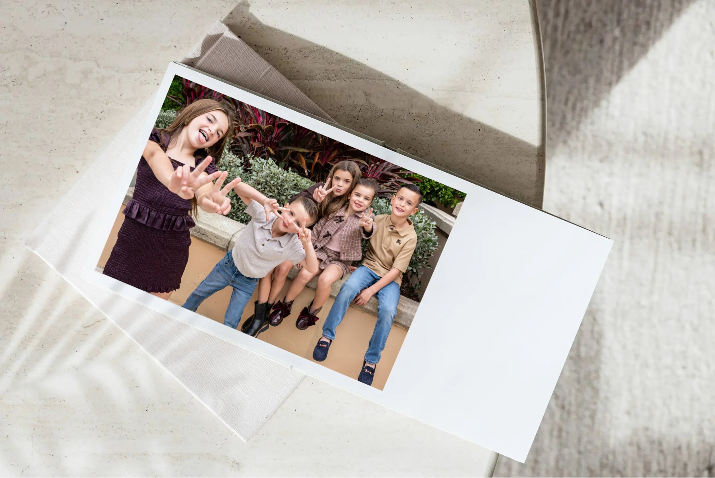A printed photo shows five children outdoors posing and making peace signs, with lush green and red plants in the background.