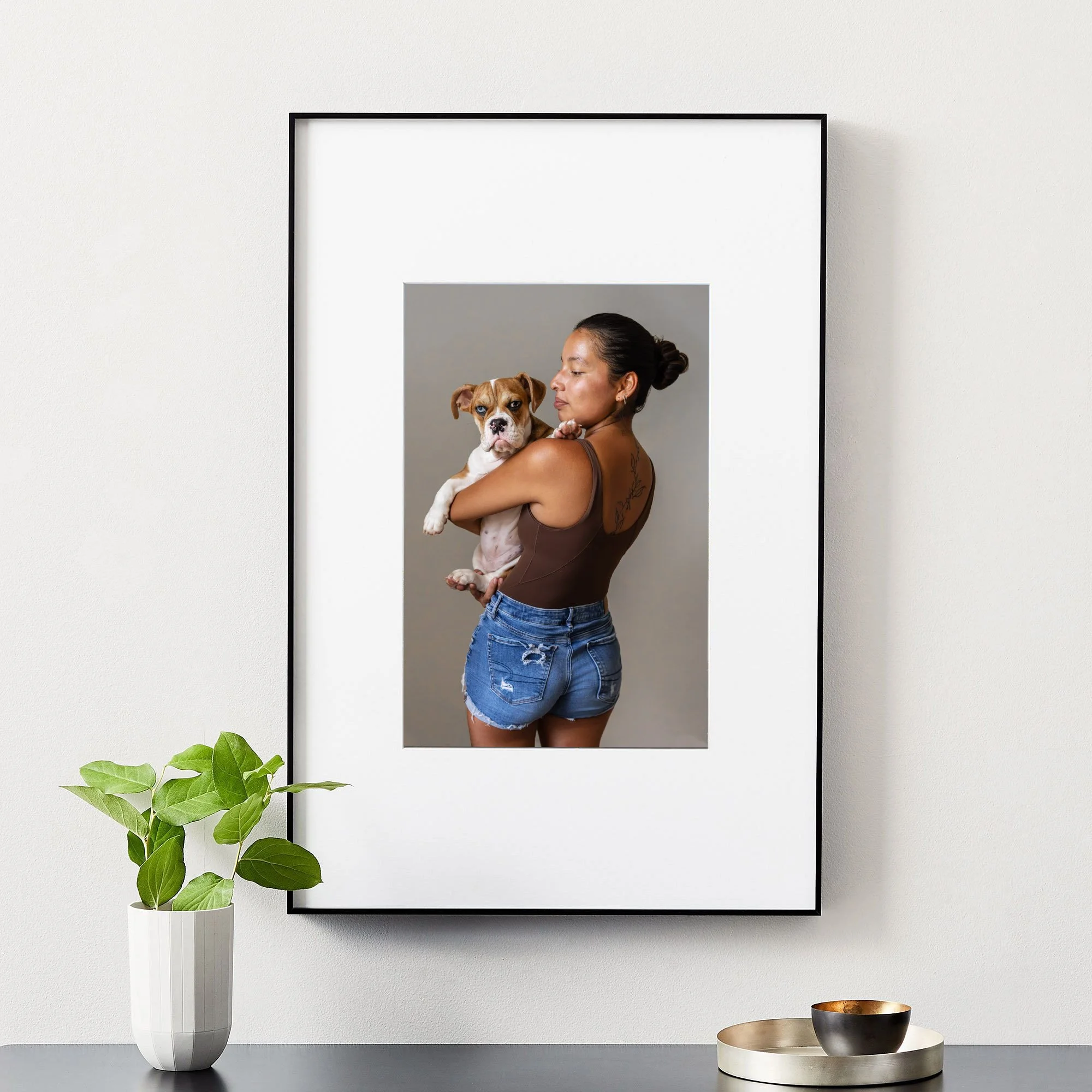 A woman holding a brown and white dog in front of a mirror, with decorative bowls and a green plant in a vase on a table nearby.