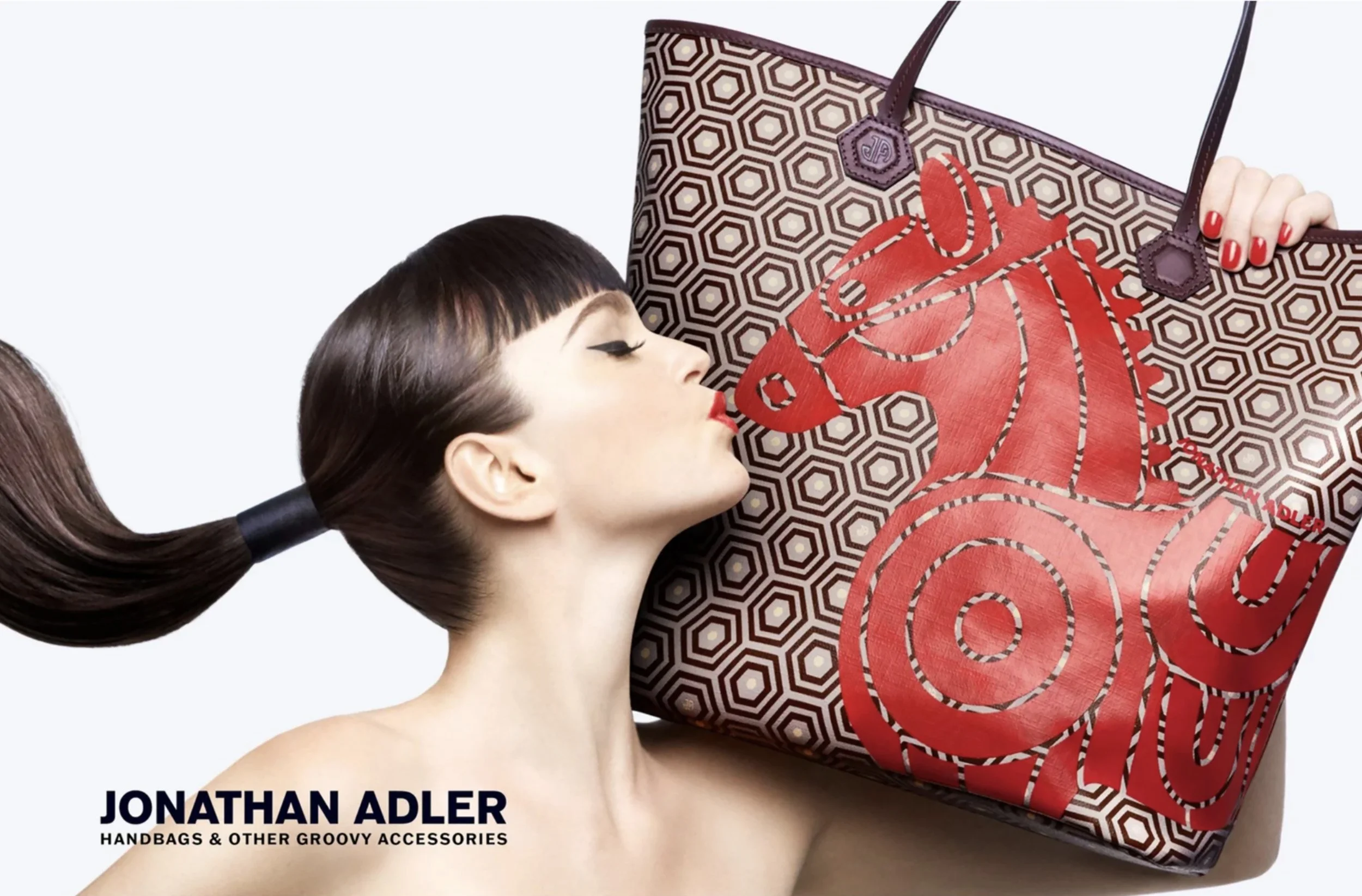 Close-up of a woman with dark hair and bangs holding a large patterned handbag on her shoulder, with her eyes closed and lips slightly puckered.