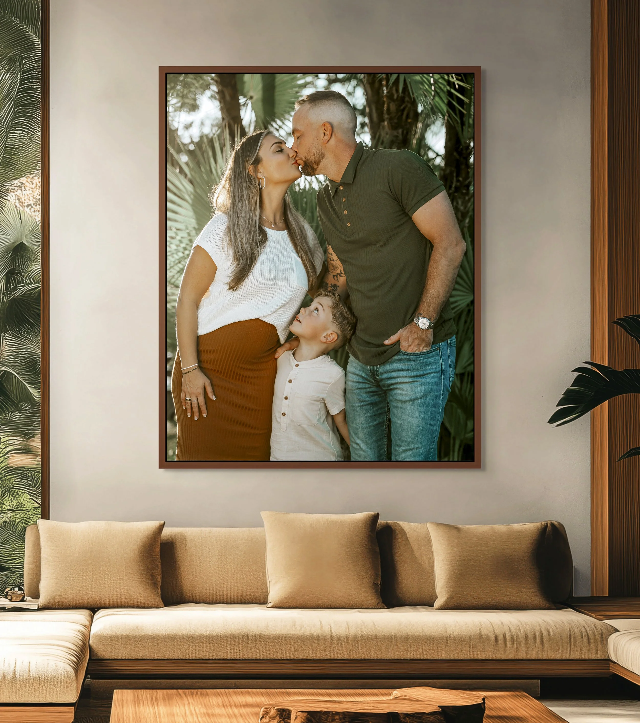 A large beige sofa with five cushions in front of a framed photo of a kissing couple and a child, hanging on a gray wall. The room has plants and wooden accents.