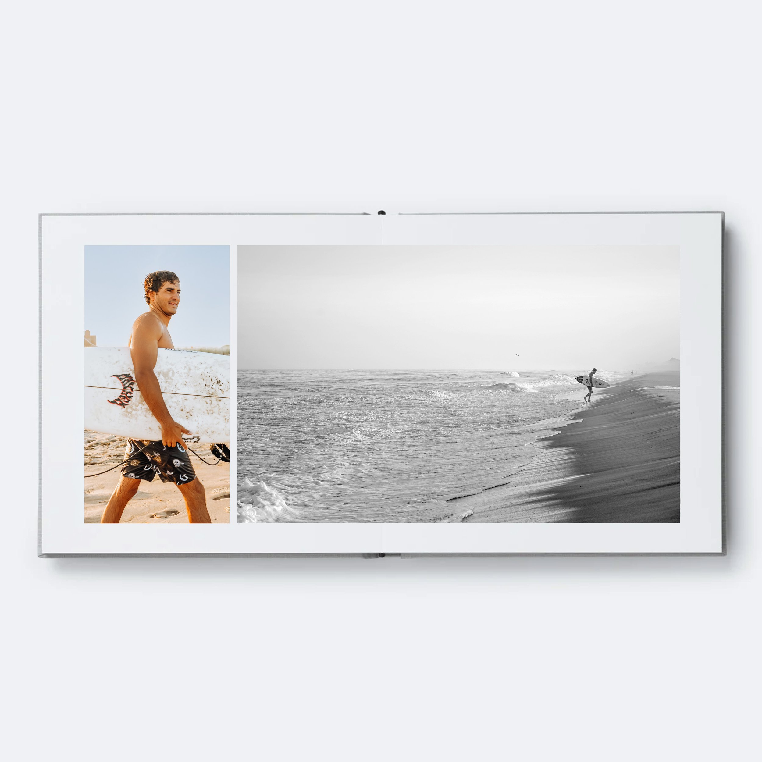A smiling man with curly hair standing in the ocean with a surfboard, with a beach in the background.