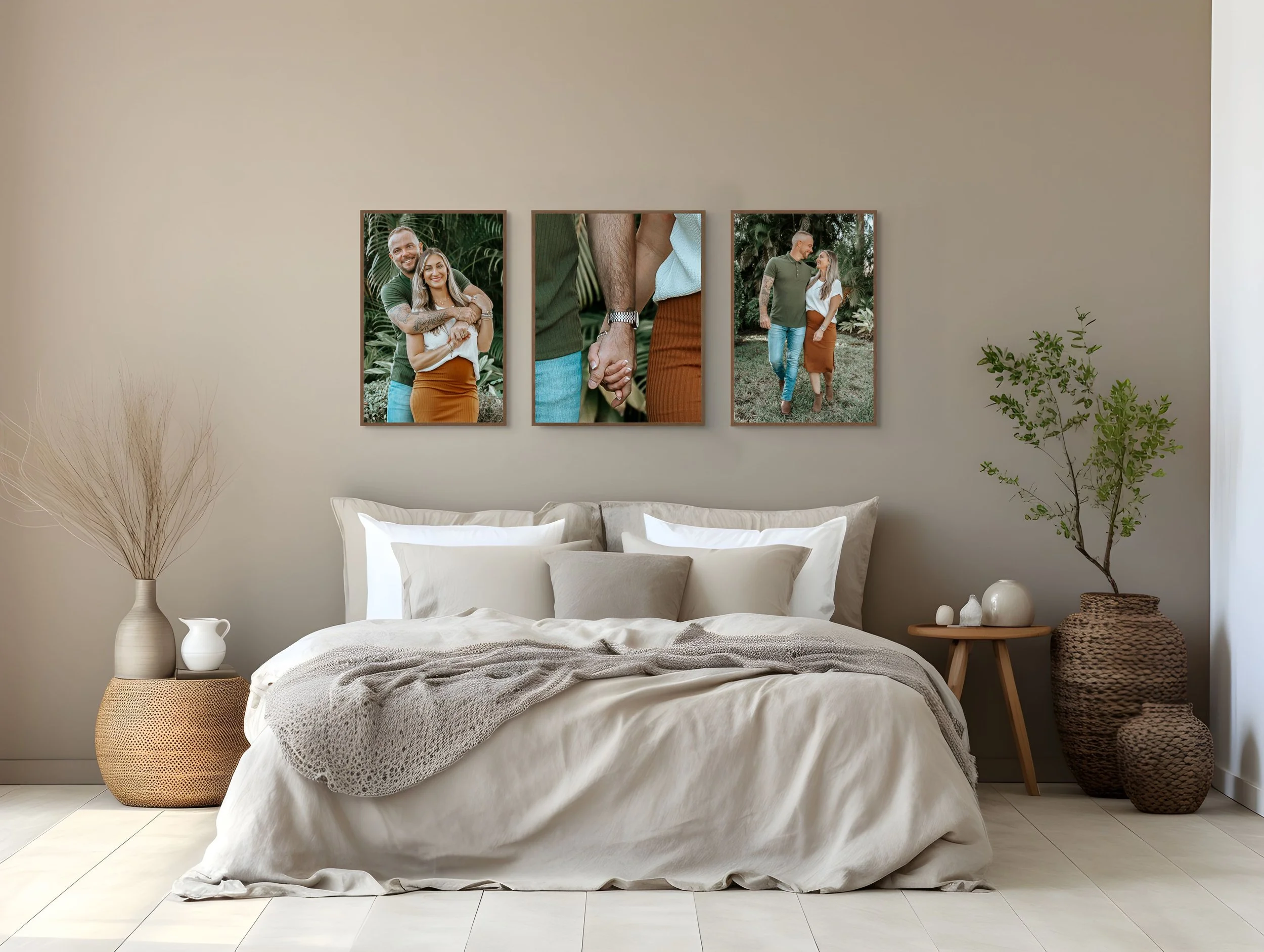 A bedroom with a bed, pillows, and a blanket. Two large woven baskets with plants and decorative objects on side tables. Three framed photos of a couple in nature hanging above the bed.