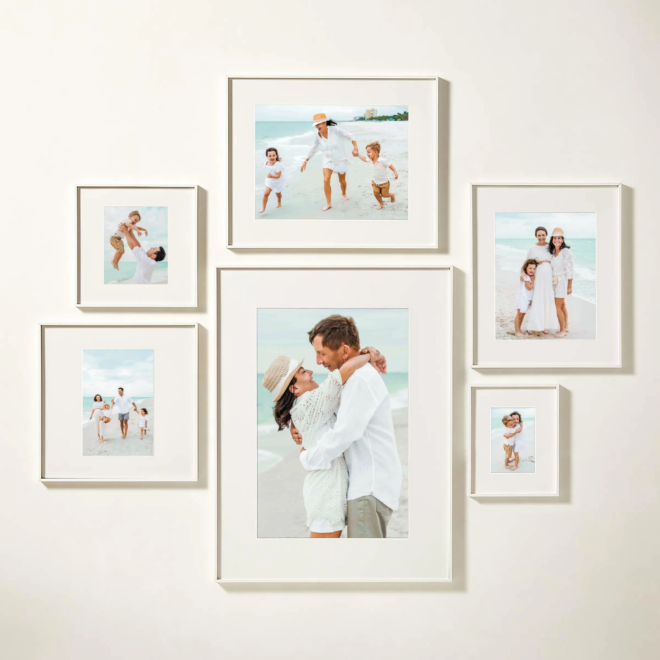 A collage of framed photographs on a white wall showing a family at the beach, including a woman in a white dress and a man holding a child.