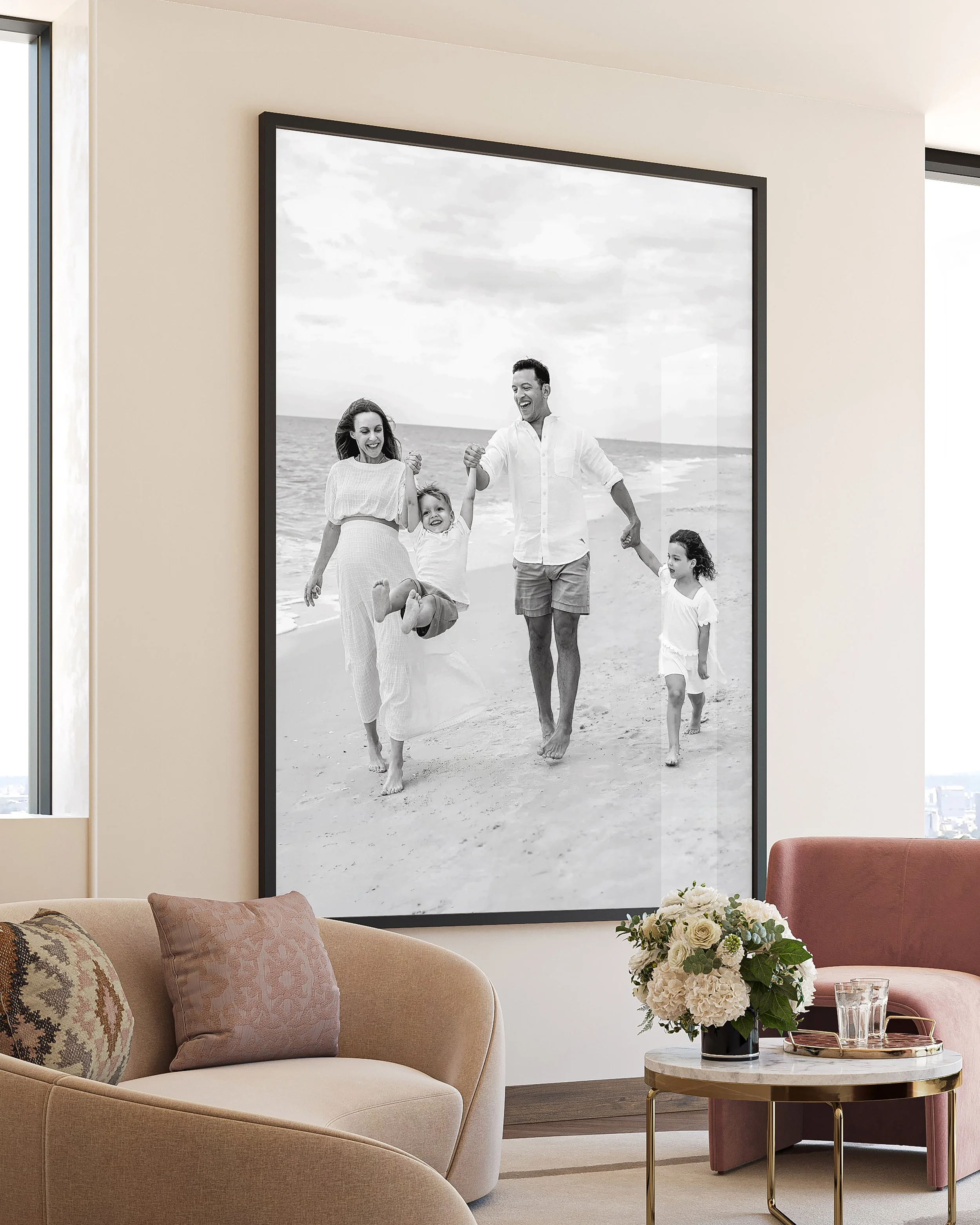 Black and white photograph of a family enjoying a day at the beach, with three adults and two children, on a large framed wall art in a living room.