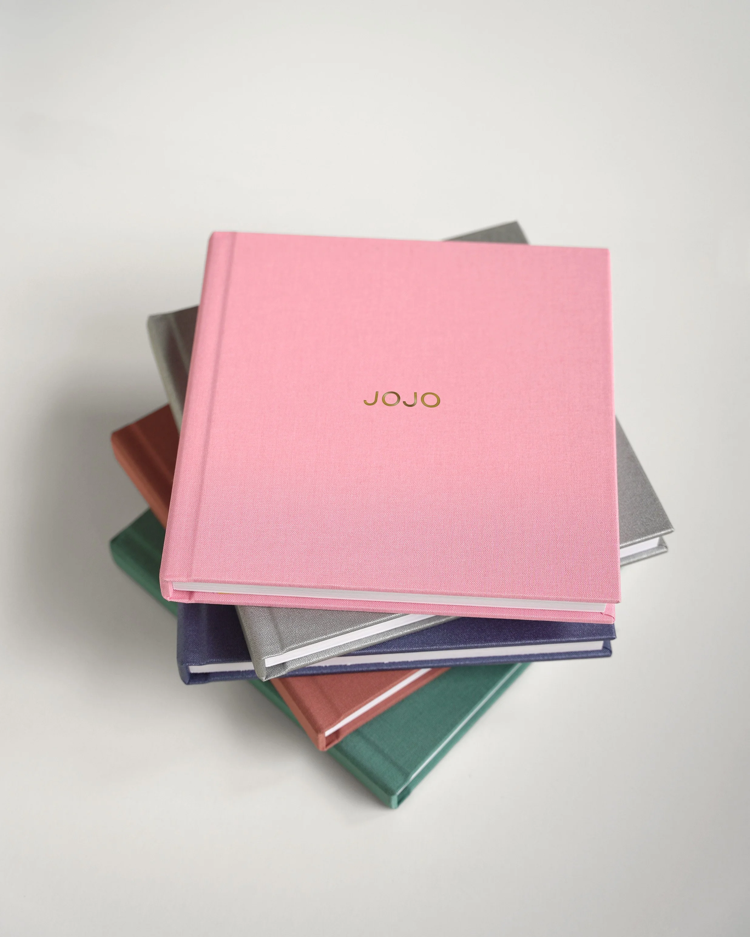 Stack of five colorful books, with a pink book on top labeled 'JOJO', on a white surface.