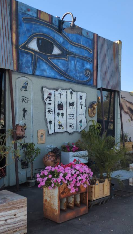 Street decor with Egyptian-themed artwork, including an eye symbol and hieroglyphs, surrounded by potted plants and flowers.