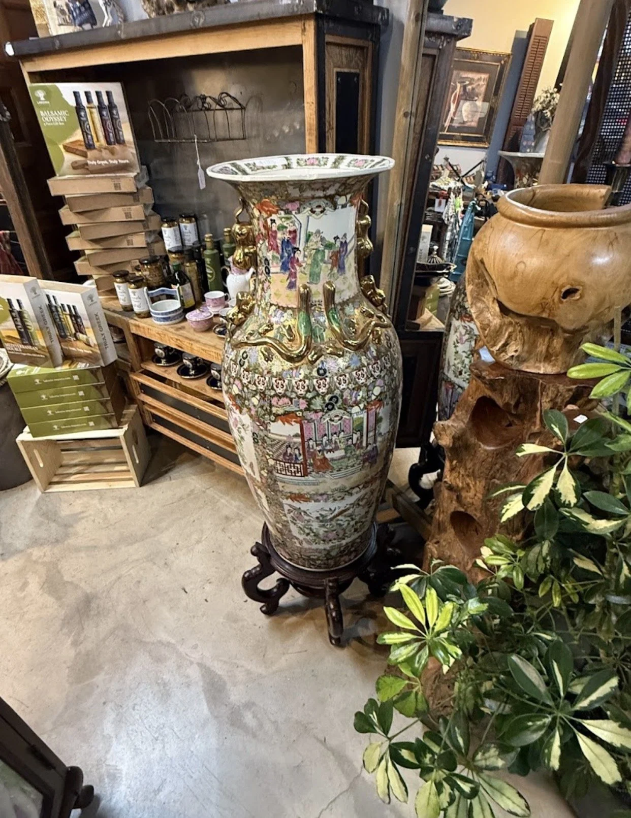A decorative Chinese porcelain vase with traditional Chinese artwork, gold embellishments, and dragon handles, placed on a wooden stand in an antique shop.