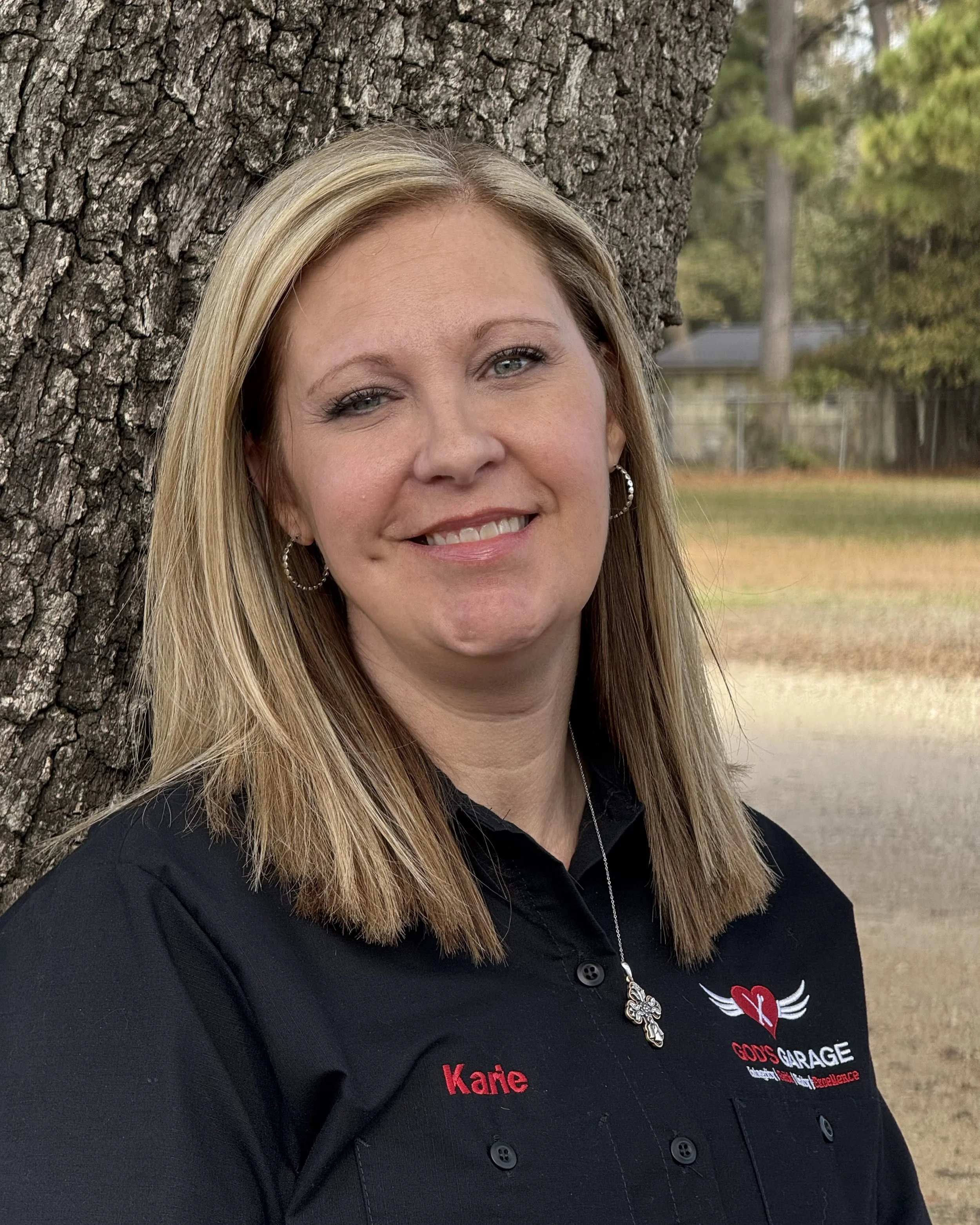 A woman with short blonde hair smiling, sitting in front of a shelf with hats.