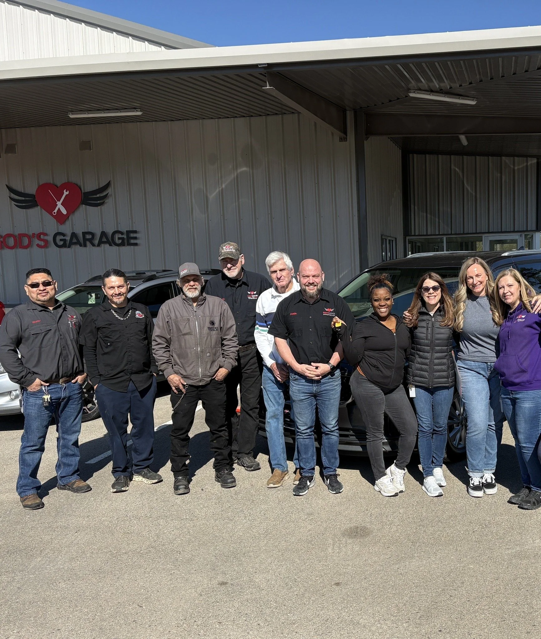 Group of ten people standing in front of a building with a sign that says 'God's Garage'.