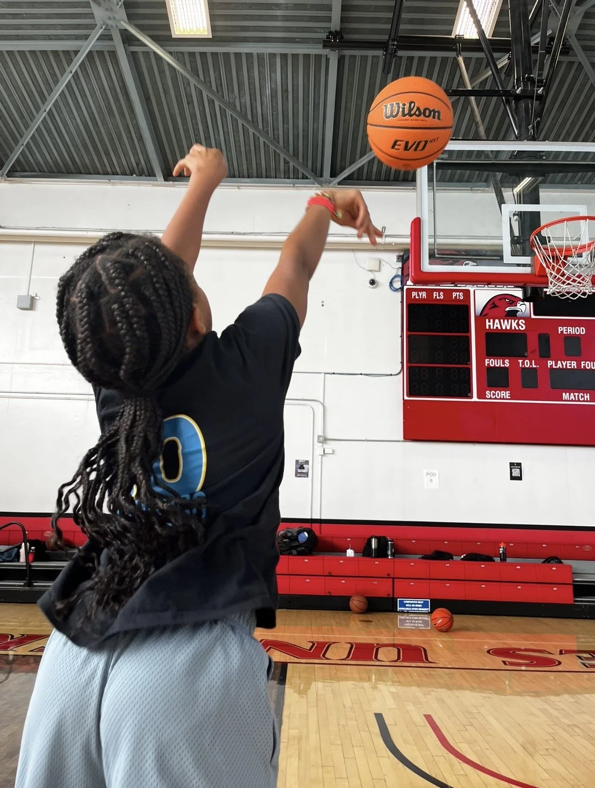 A young girl is shooting a basketball at the hoop in an indoor gymnasium.