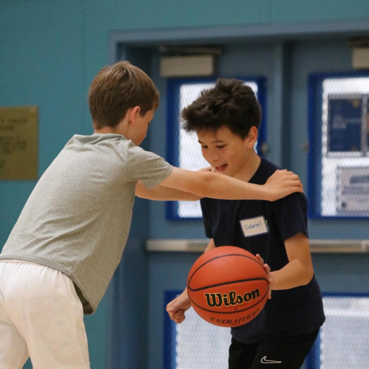 Two boys playing basketball indoors; one boy is passing the ball to the other.