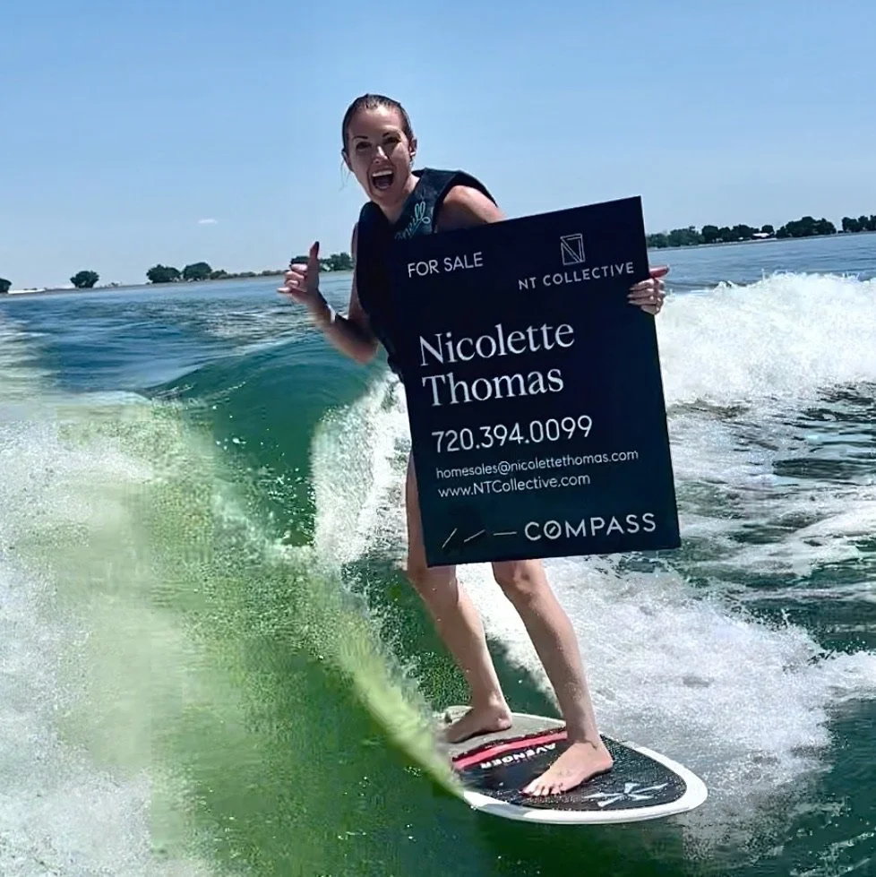 Laid back realtor Nicolette Thomas wakeboarding while holding a "For Sale" real estate sign